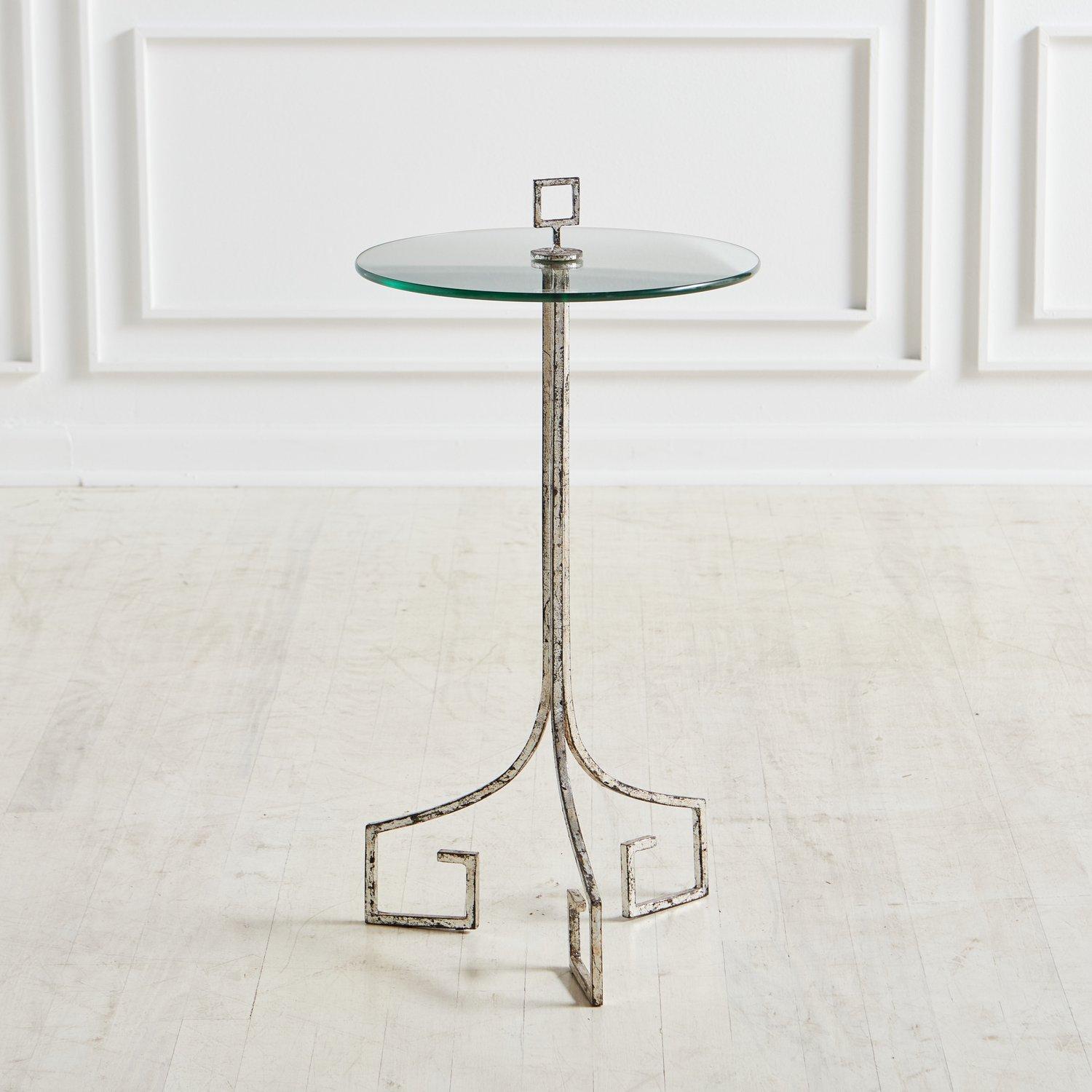 A beautiful mid-century occasional table featuring an angular tripod metal base with a .375” thick circular glass table top. The metal base has a hand applied silver leaf finish and the table top is held in place by a square handle, making it easy