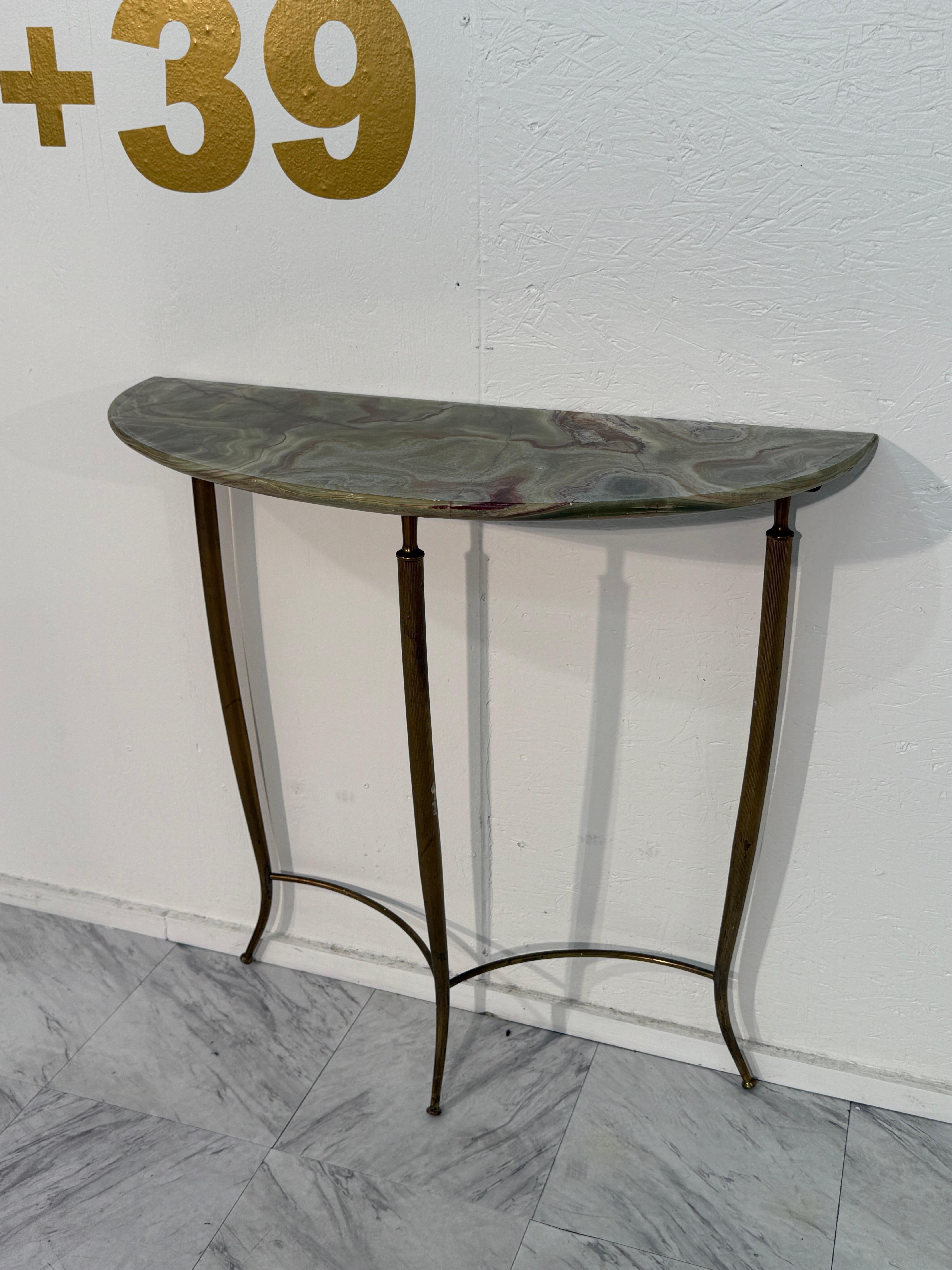 Elegante consolle italiana della metà del secolo scorso con un piano in onice riccamente decorato nei toni del verde, del crema e del bordeaux, posto su una sottile base in ottone. La forma demilune (a mezzaluna) del tavolo lo rende ideale per