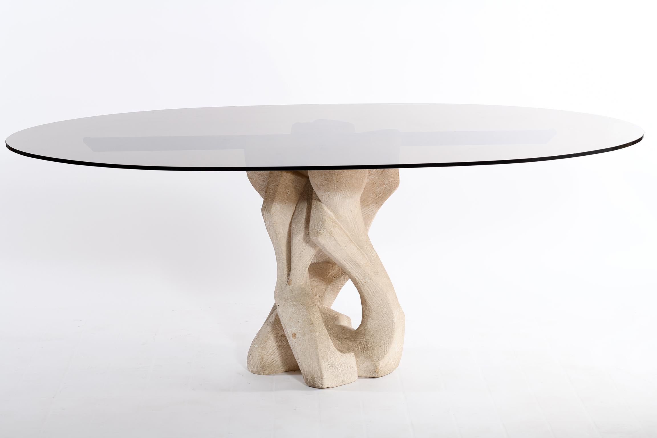 Dining table or center table, large console with oval top in thick smoked glass resting on an abstract Brutalist sculptural base in stone agglomerated, in the upper part the sculpture base we find a bronzed brass bar that helps support the large top