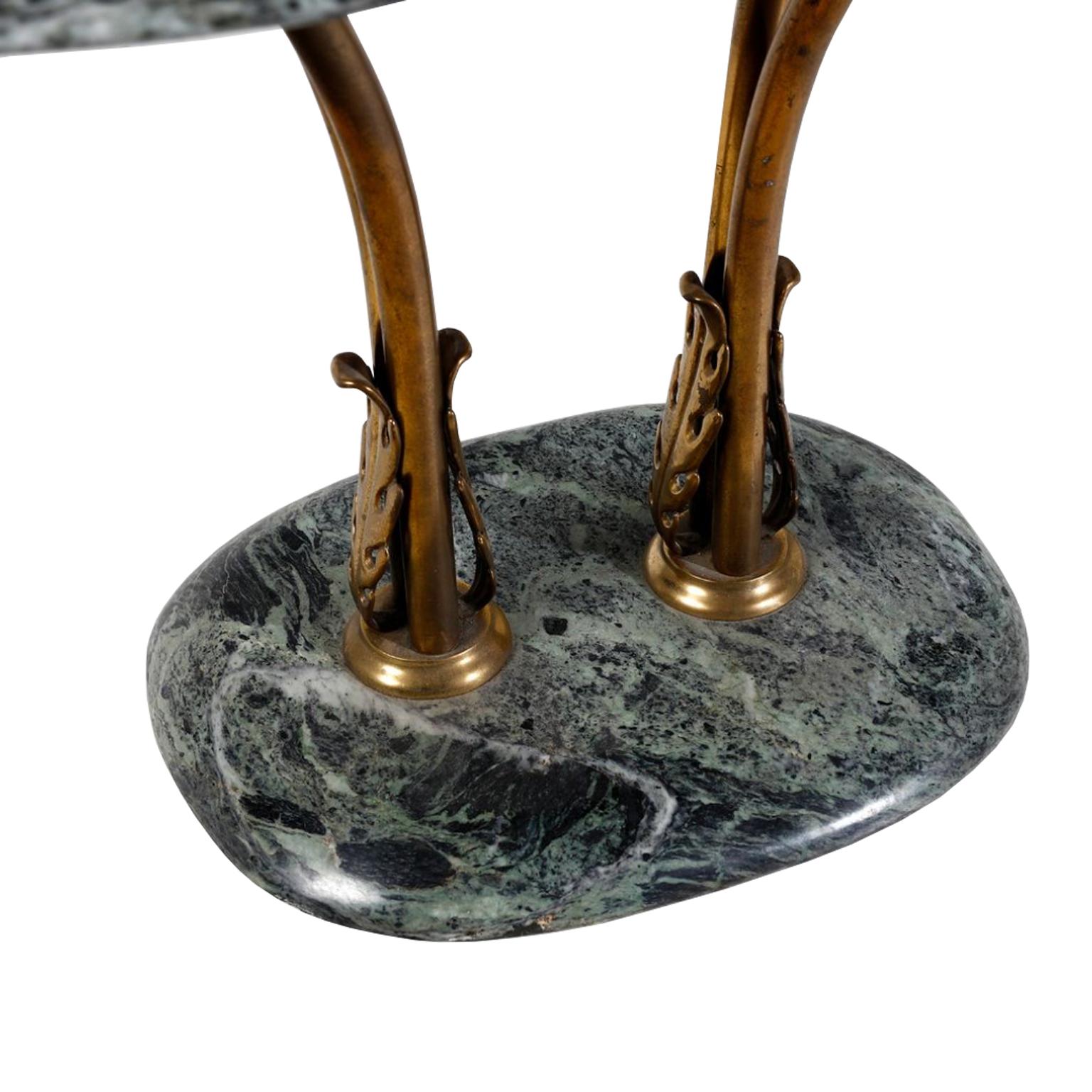 Ovaler Beistelltisch Vintage mit Platte und Sockel aus grünem Marmor.  Dieses Möbelstück hat bronzefarbene Metallbeine, die auf beiden Seiten ein stilisiertes Blattmotiv hervorheben.  Die Oberseite der Beine wölbt sich übermäßig, um die ovale
