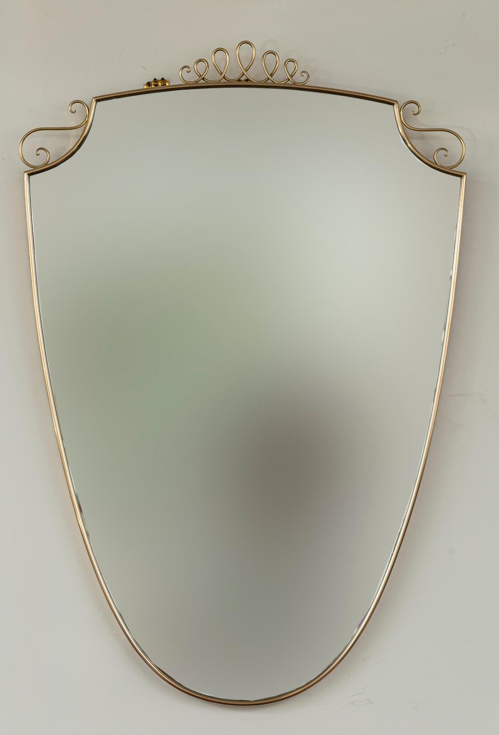A classial Gio Ponti designed unlacquered brass mirror originally made in the 40's, this later 20th century version is charming and shown with scrolls as its crown and then s-shaped scrolls flank its chamfered sides. Mirror composed of a solid