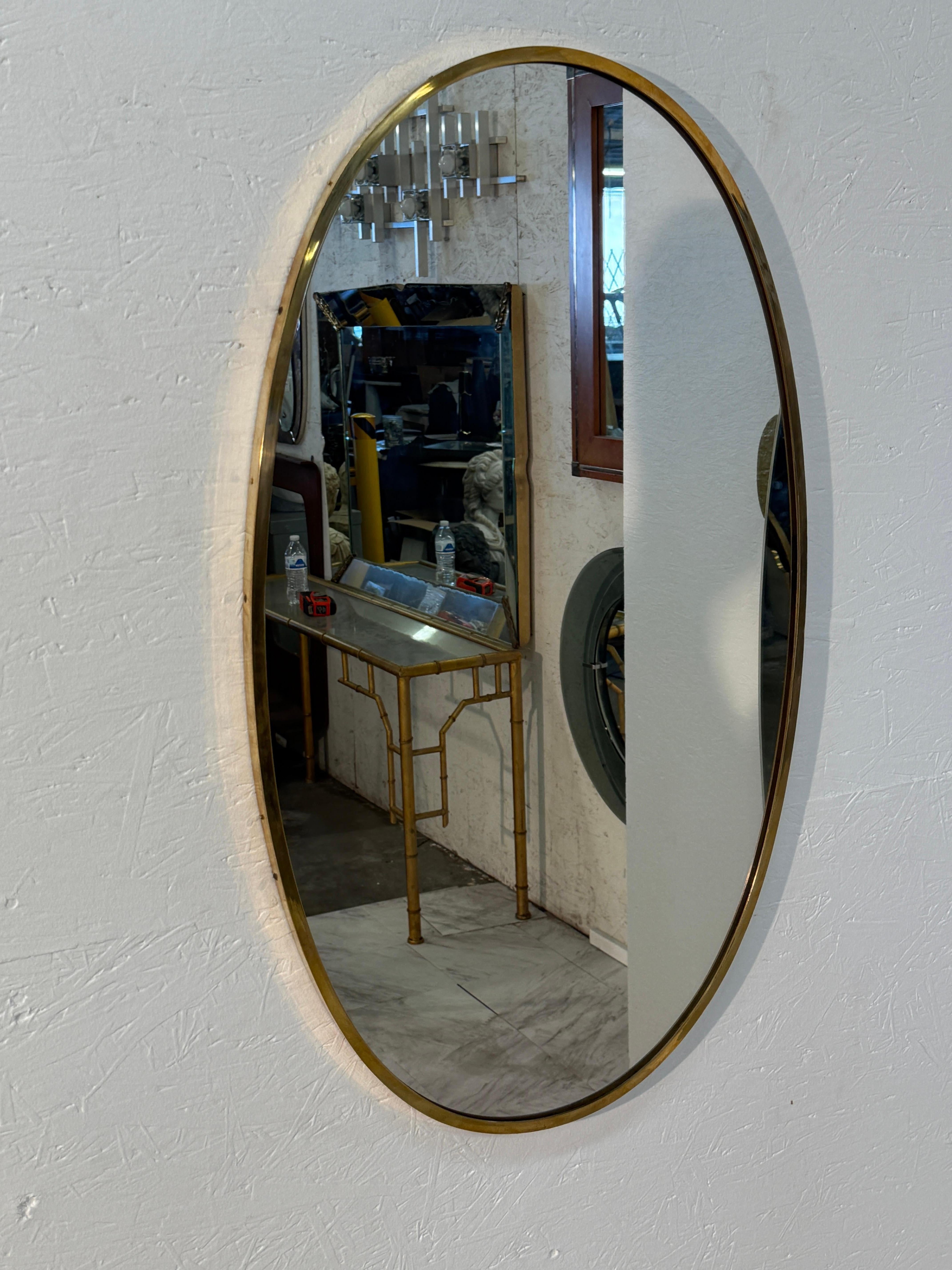 Ce miroir mural ovale italien raffiné du milieu du siècle présente une élégance intemporelle avec sa forme allongée et son cadre en laiton chaleureux. Le bord mince et arrondi embrasse le miroir avec une sophistication discrète, soulignant la pureté