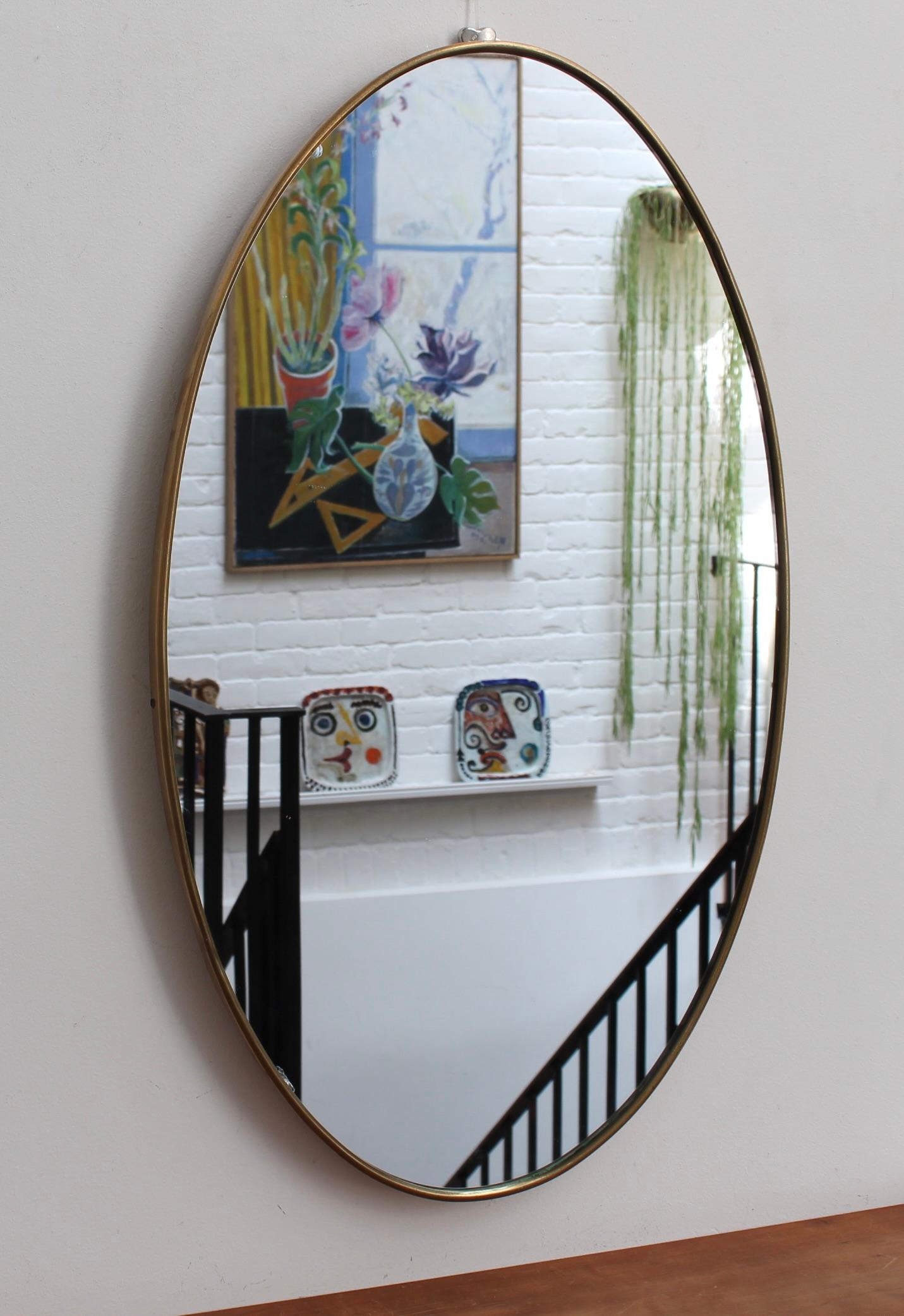 Mid-century Italian oval wall mirror with brass frame (circa 1950s). The mirror is oval in shape and very smart with irresistible durability. The visual impression is elegant and very distinctive in a modern Gio Ponti style. The mirror is in