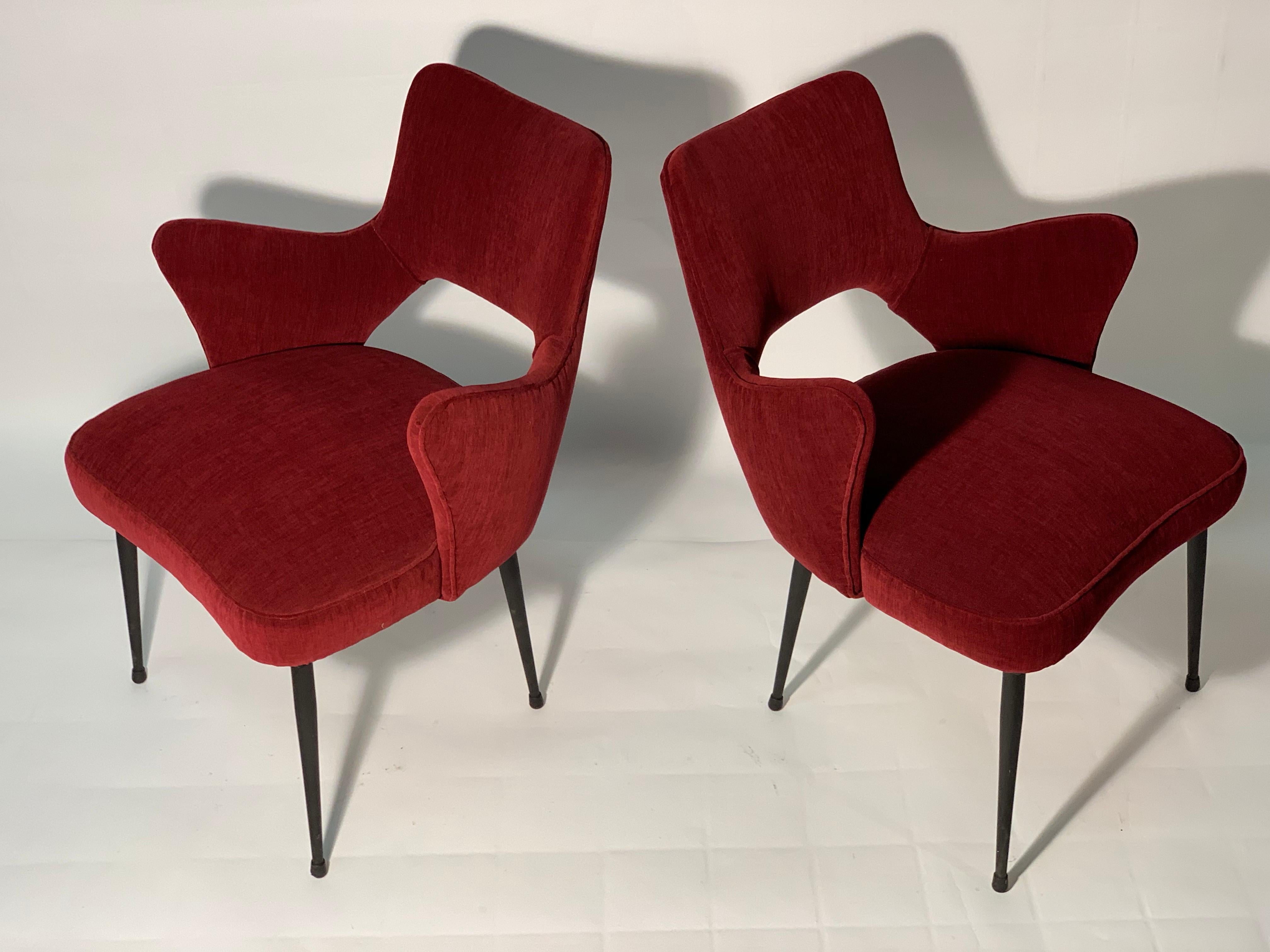 Pair of chairs with a sinuous shape covered with a new soft red cotton fabric similar to a velvet, shaped and rounded armrests, shaped seat and concave back with a hole in the lower part.
Slim legs that are lowered towards the bottom in black