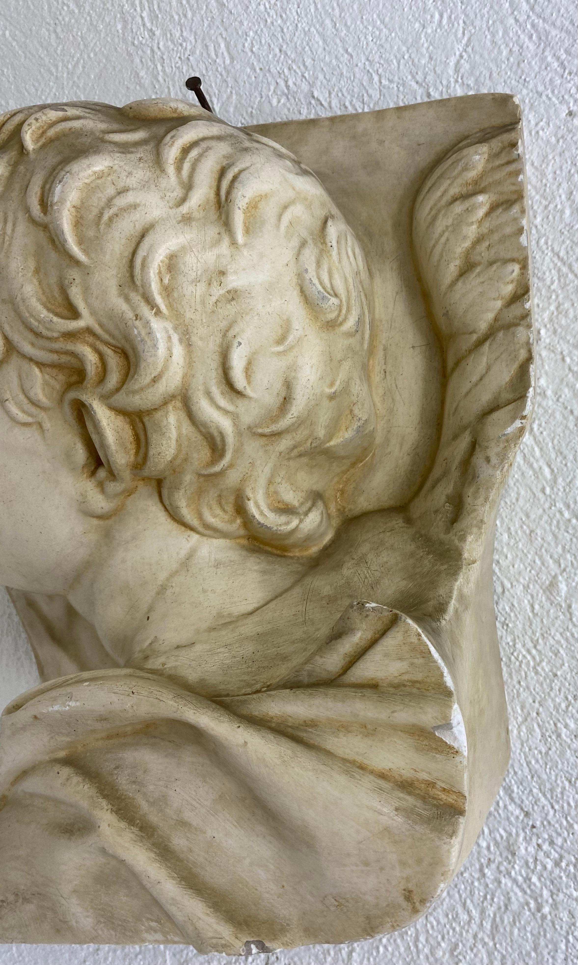 Si tratta di un congelamento in gesso vintage di metà secolo di un giovane angelo maschio. Questa scultura da parete appesa è un busto tridimensionale e presenta una patina adeguata alla sua età. Questo busto in stile barocco italiano ha il suo
