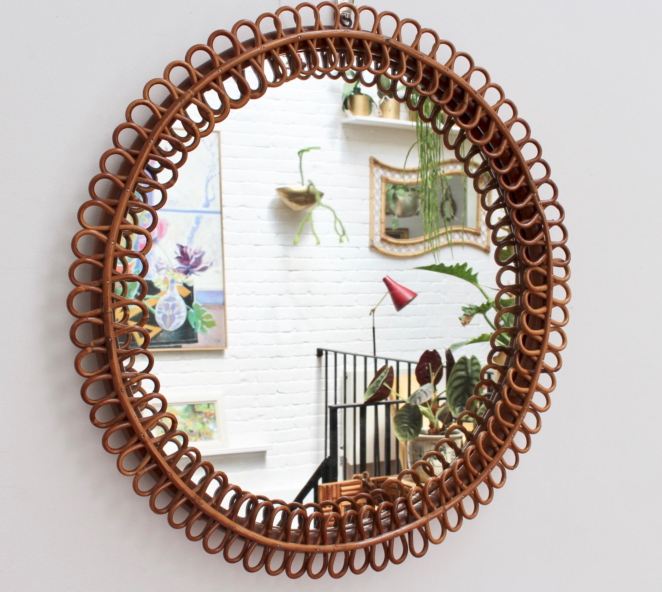 Mid-century Italian rattan round wall mirror (circa 1960s). This mirror has a very delightful circular sun-shape framed with whimsical rattan figure-eights. There is a characterful, aged patina on the mirror frame and overall, the piece is in good