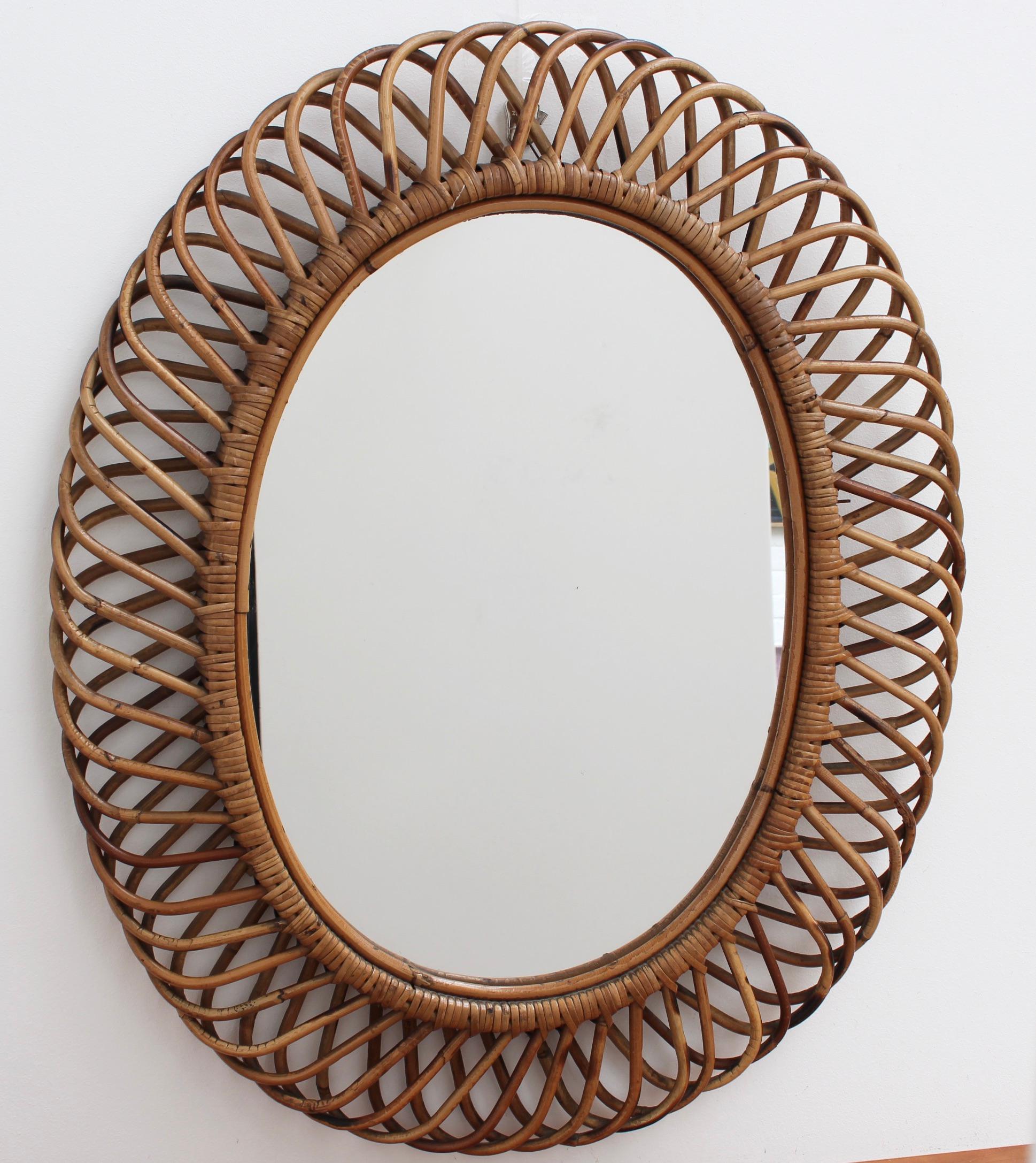 Italian rattan wall mirror (circa 1960s) in the style of Franco Albini. The mirror has a complex weave of rattan in a series of horseshoe-shaped projections on the frame edge. There is a graceful, aged patina on the mirror frame providing