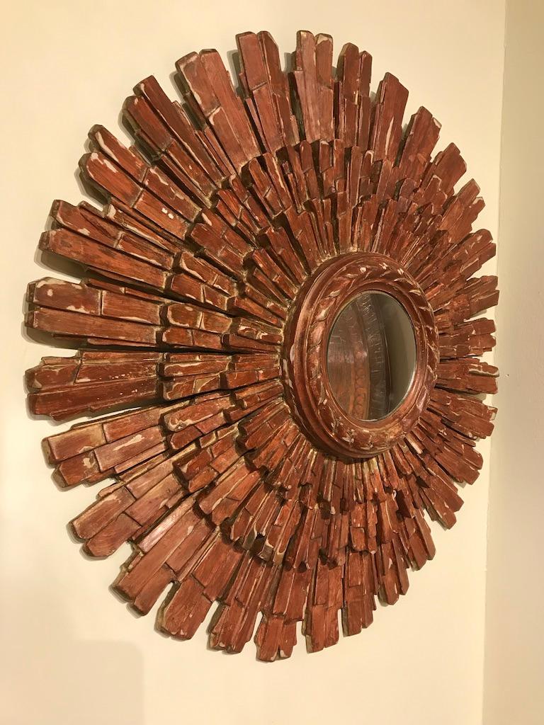 Stunning Italian hand carved wood starburst mirror in red bol. Originally gilded, now worn down to the red base, 'bol', that the gilding is set on, it makes for a unique color and surface. The multilayered hand carving gives this piece a lot of