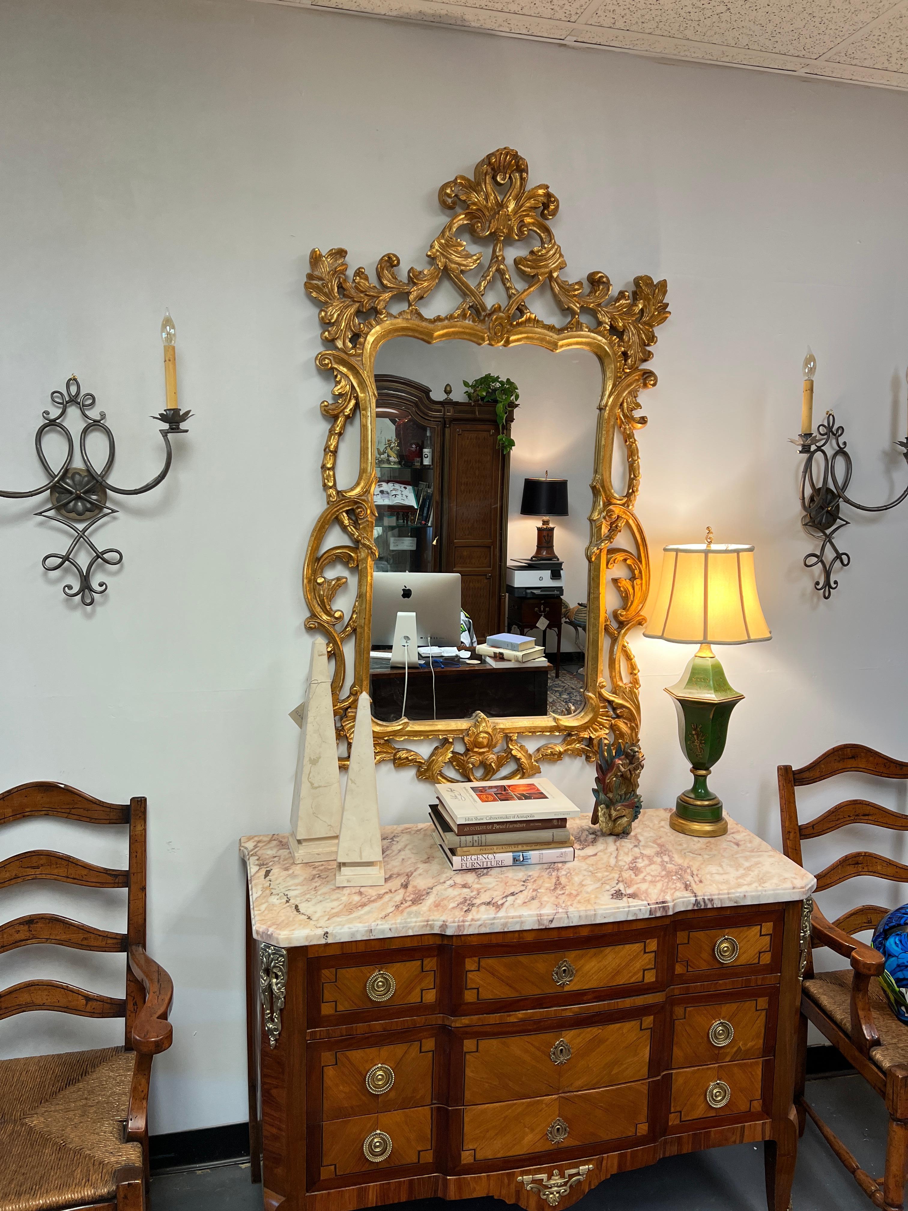 Here is featured a large Italian hand carved gilt wood mirror or looking glass in the Rococo style. This mirror was manufactured circa 1950-1960. The frame is made from fruit wood and completely hand carved. The carvings are crisp and distinct. The