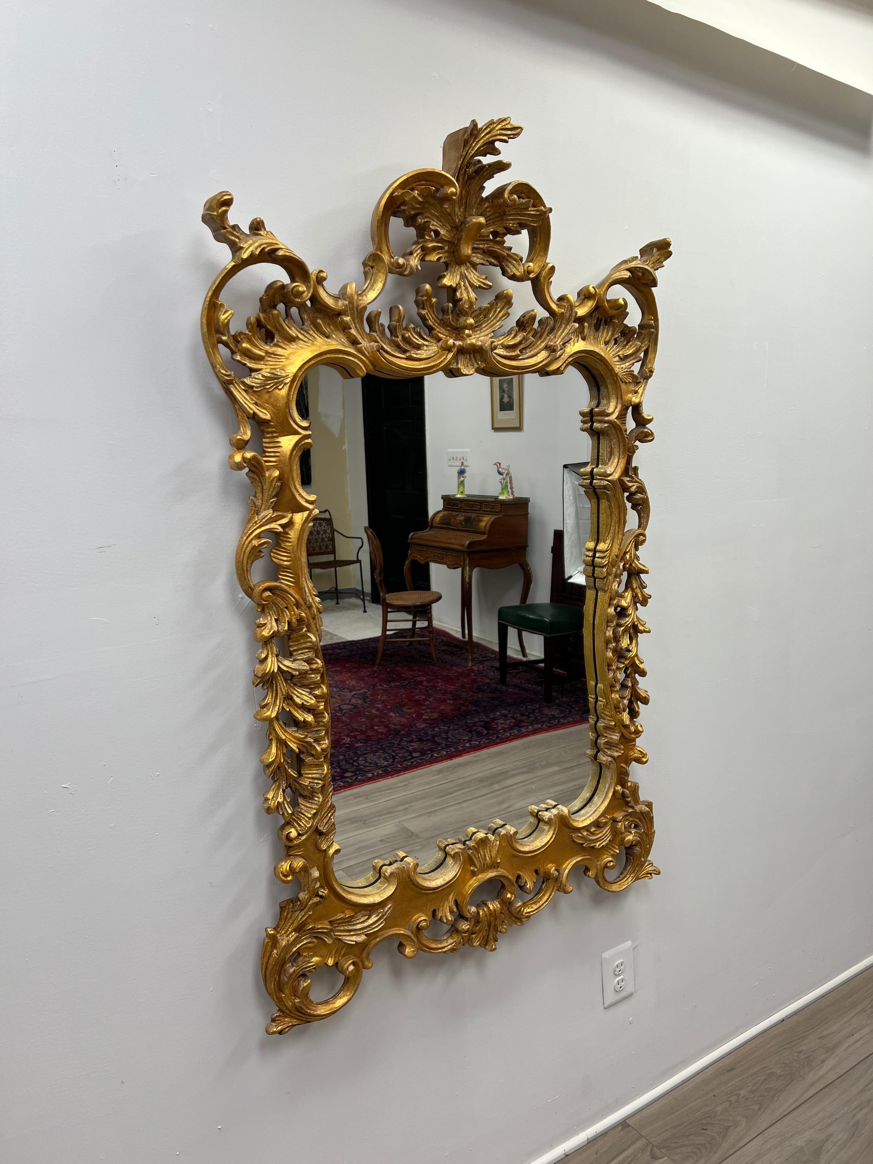 Here is featured a large Italian hand carved gilt wood mirror or looking glass in the Rococo style. This mirror was manufactured circa 1950-1960 in Italy for Debarge Mirrors. The frame is made from fruit wood and completely hand carved. The carvings