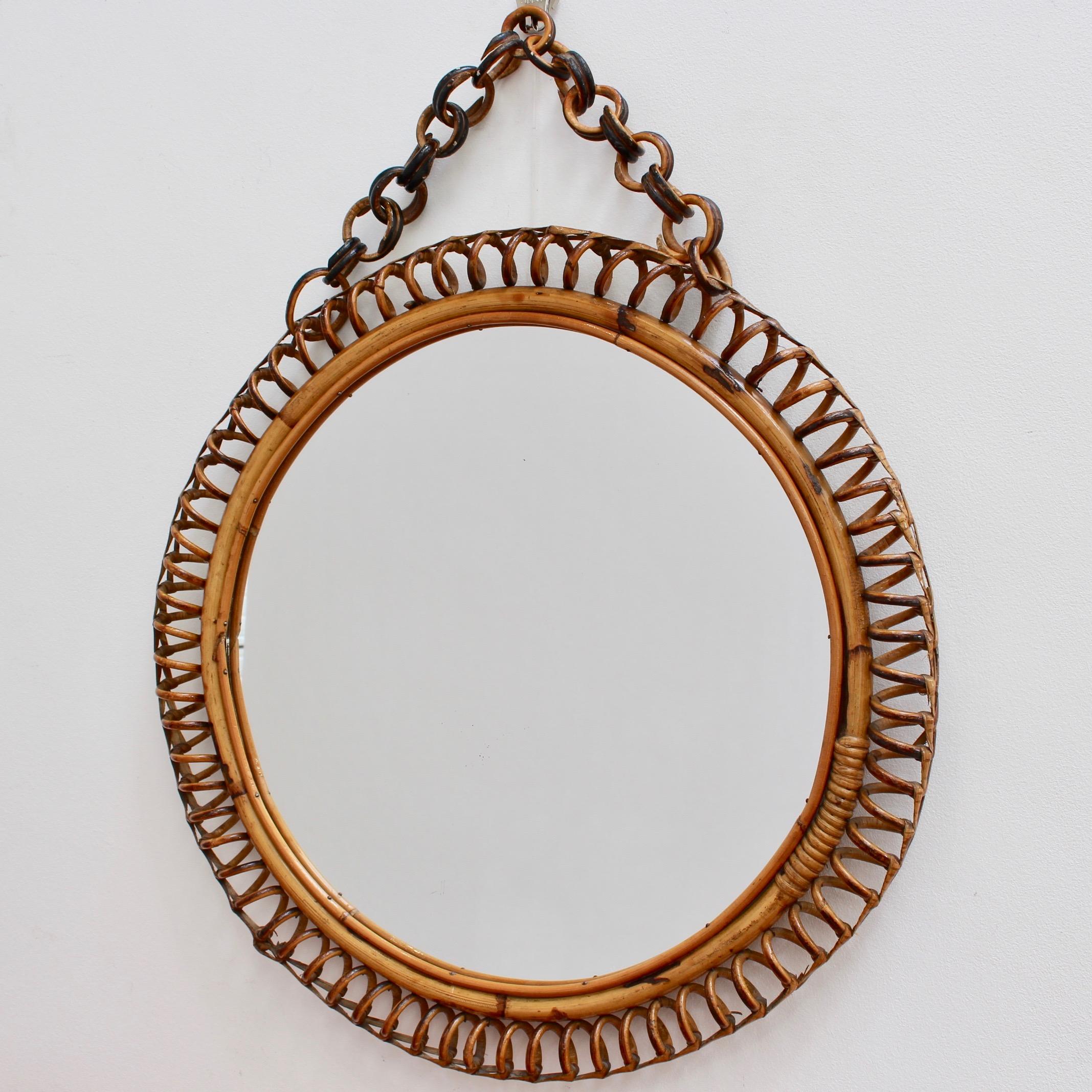 Italian circular-shaped rattan wall mirror (circa 1960s). This mirror has a very charming Classic shape with rattan spirals framing the mirror. The rattan hanging chain adds further allure. There is a characterful, aged patina on the mirror frame