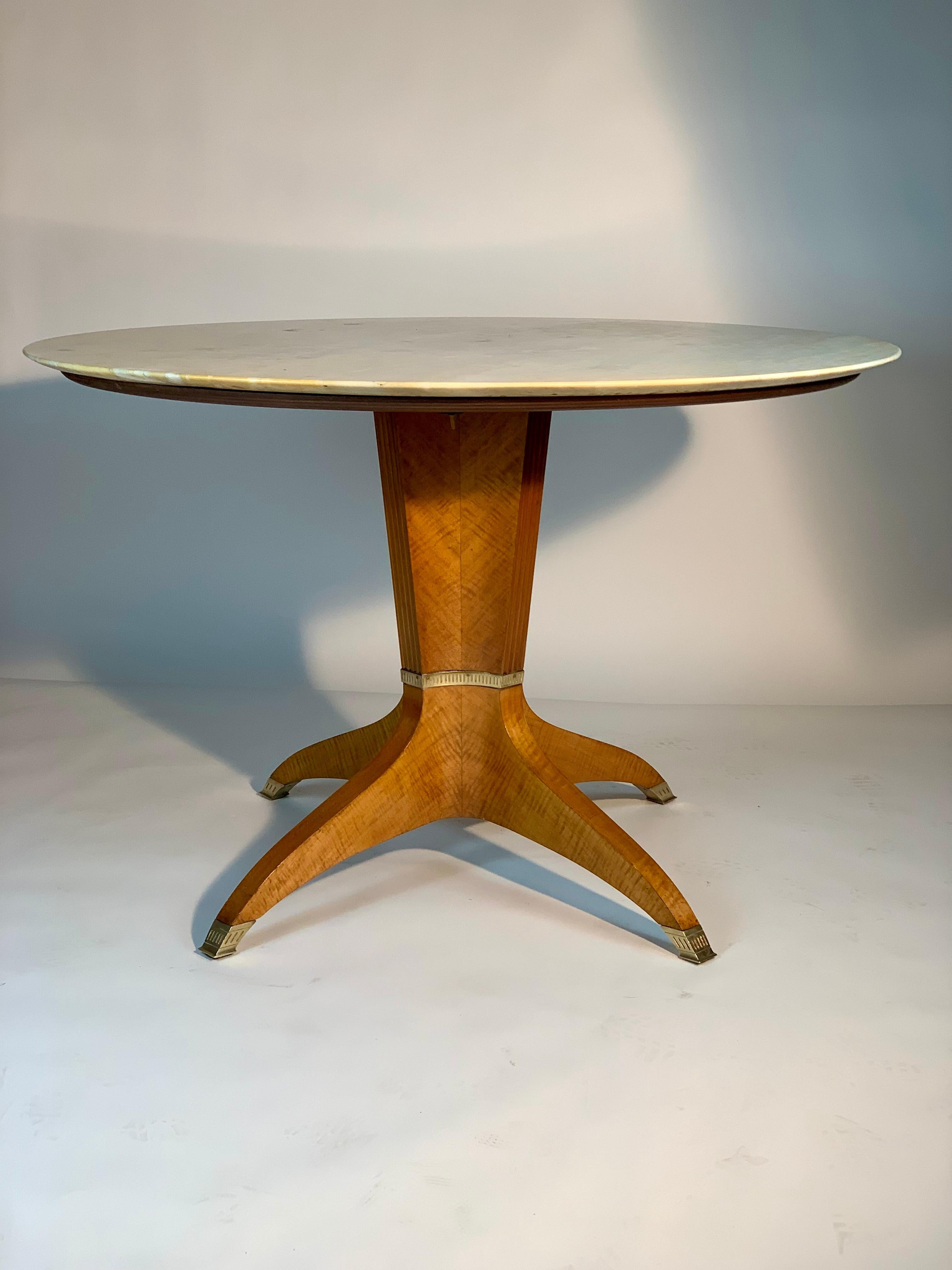 Mid-century Italian round table with light colored marble top and rounded edge, four-lobed base each element with grooved front side and details in cast brass that turn around and form a sort of band, from the base four legs extend curved towards