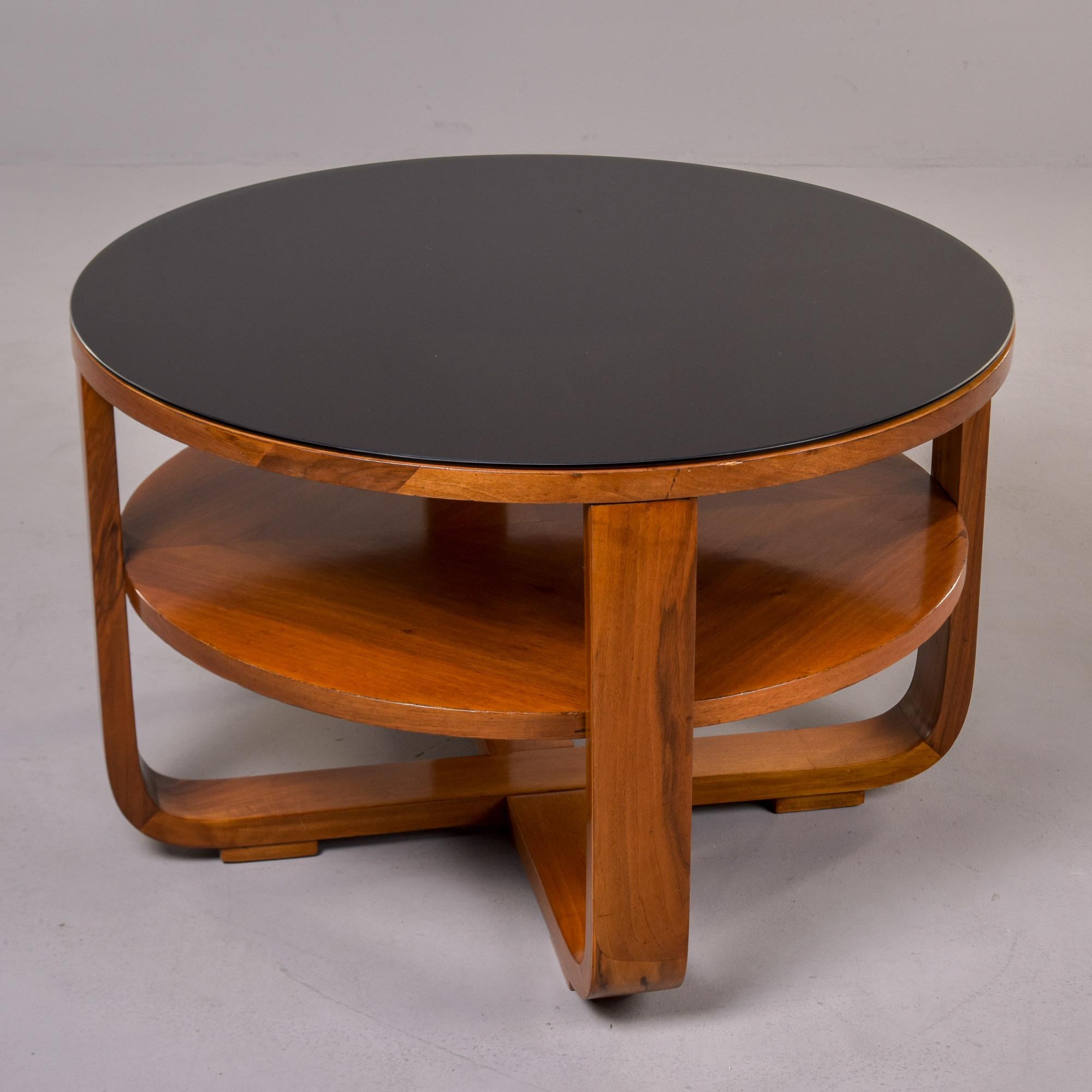 Trouvée en Italie, cette table ronde d'appoint ou de cocktail date des années 1950. Fabriquée en noyer, cette table comporte deux plateaux ronds soutenus par une base en X à pieds courbés. Nouveau plateau en verre noir taillé sur mesure. La finition