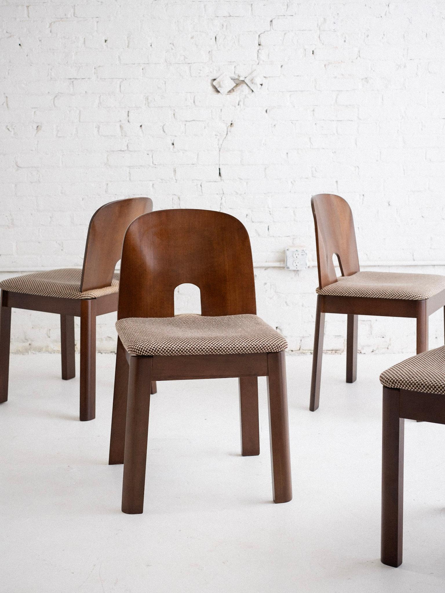 A set of four mid century Italian dining chairs in the style of Tobia Scarpa. These chairs have a minimalist design with a slightly curved wooden backrest. The cutout near the bottom serves as a visual accent and practical handle. The seat cushion