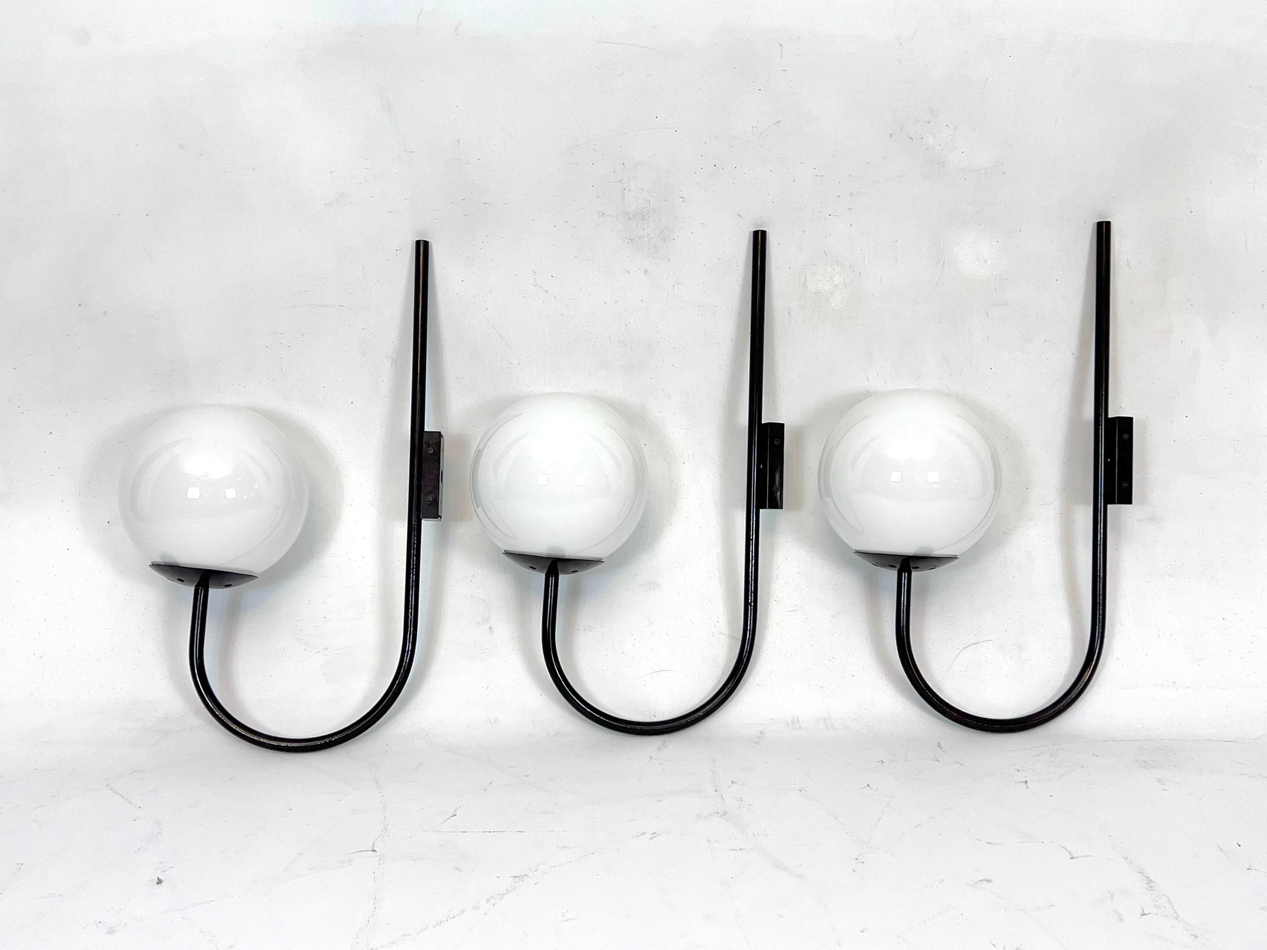 Manufactured in Italy during the 60s, these large sconces are made from milk glass and black lacquered metal. In original vintage condition with normal trace of age and use. No cracks or chips on the glasses. Full working with EU standard, adaptable