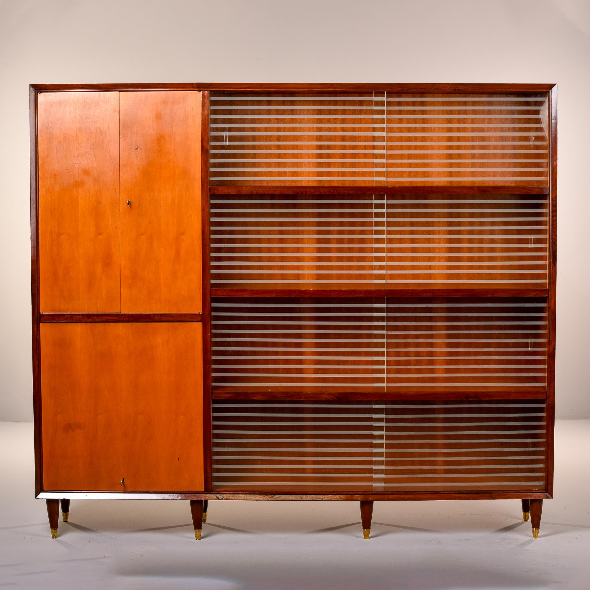 Found in Italy, this circa 1960s shelf cabinet stands over five feet high and is nearly six feet wide. Supported by eight tapered and brass-capped legs, this cabinet has a section of shelves with three fixed shelves behind sliding etched glass