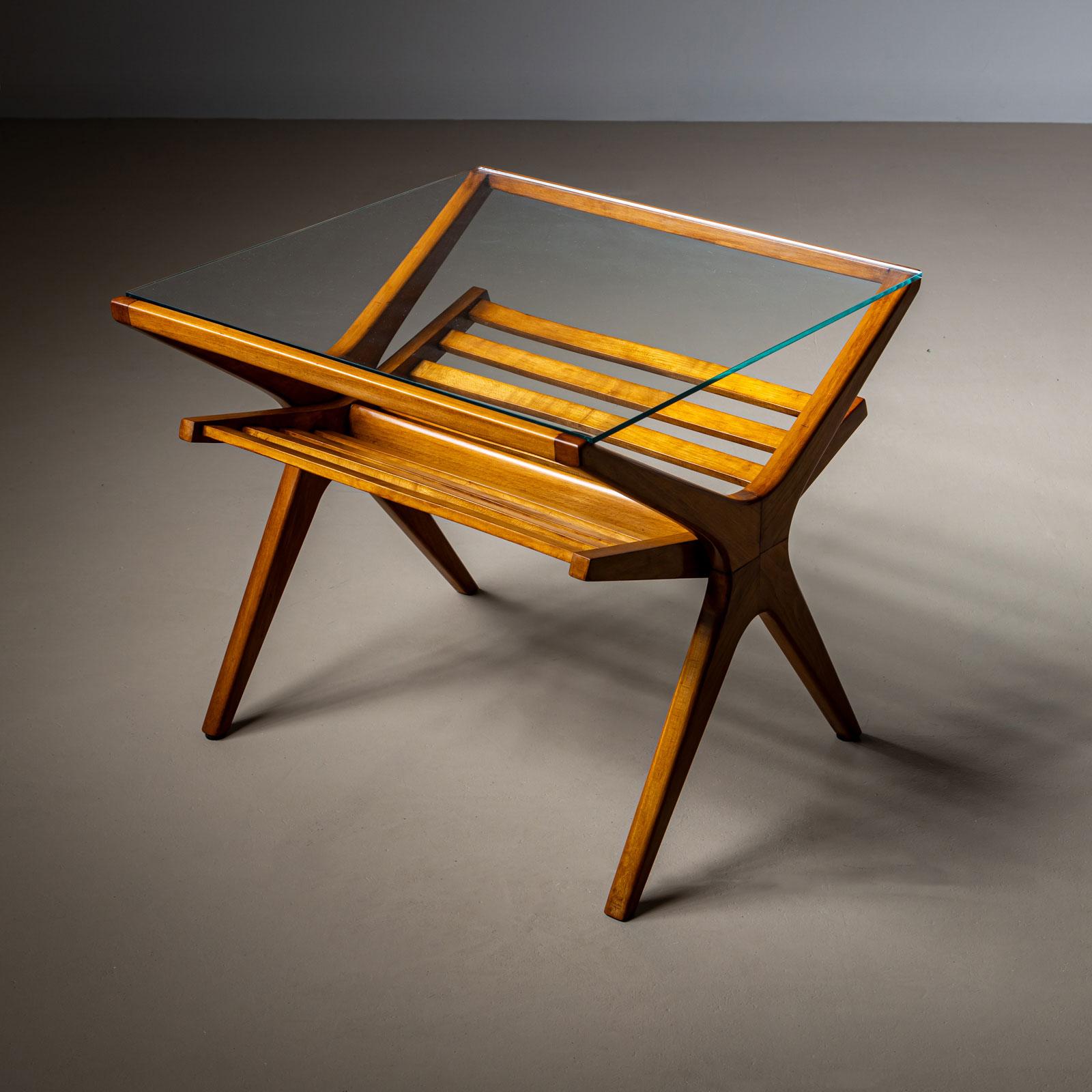 Une élégante table d'appoint italienne du milieu du 20e siècle, dotée d'un cadre en bois lisse et d'un plateau en verre épuré. La structure en X de la table crée un profil accrocheur, tandis que le porte-revues intégré sous la table offre un