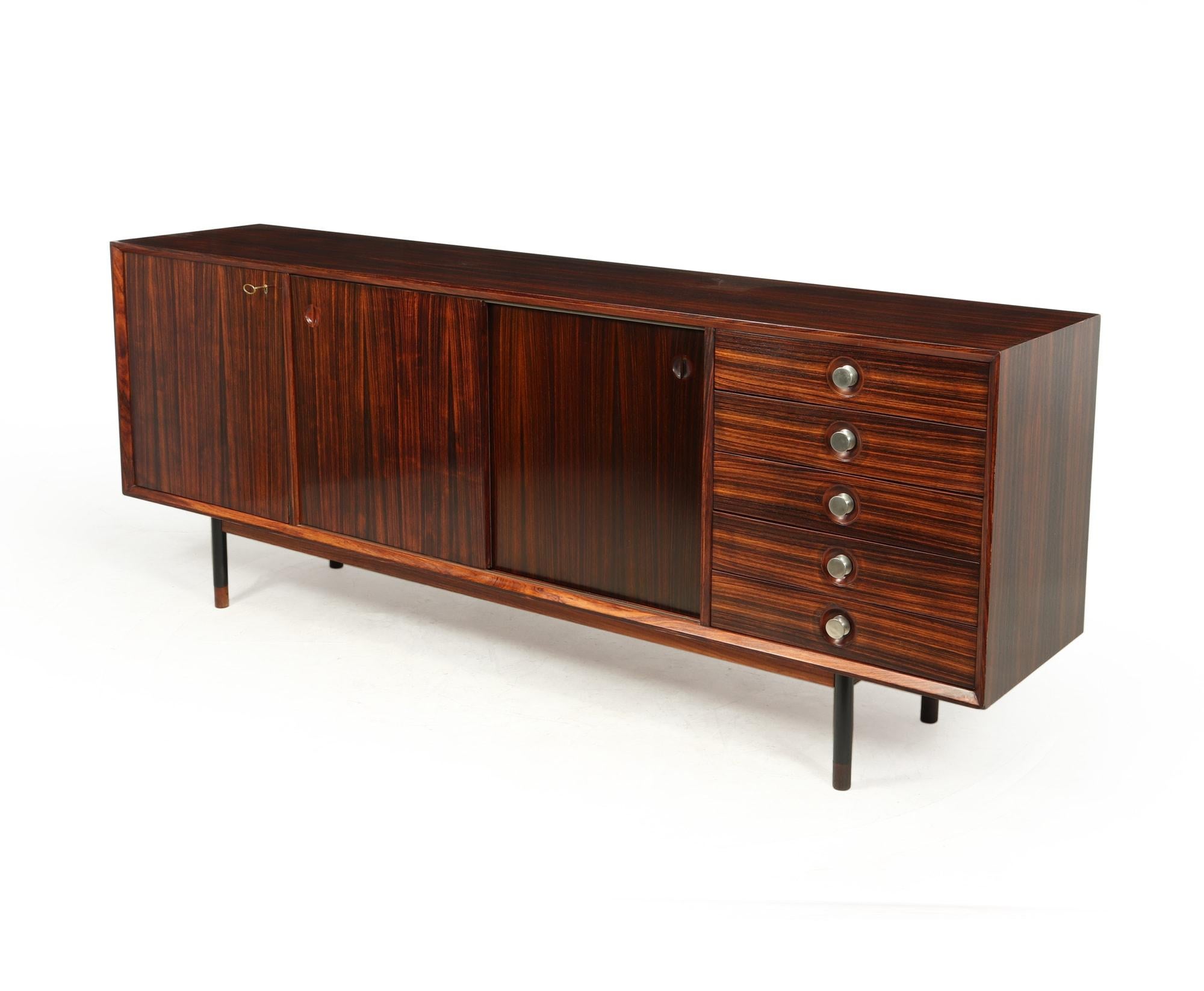 A Mid-Century Modern long sideboard produced in Italy in the 1960’s by cabinetmakers Faram, it has reversible center drawers ( white one side rosewood the other), five drawers to the right with chrome plated handles and lockable door to the left,