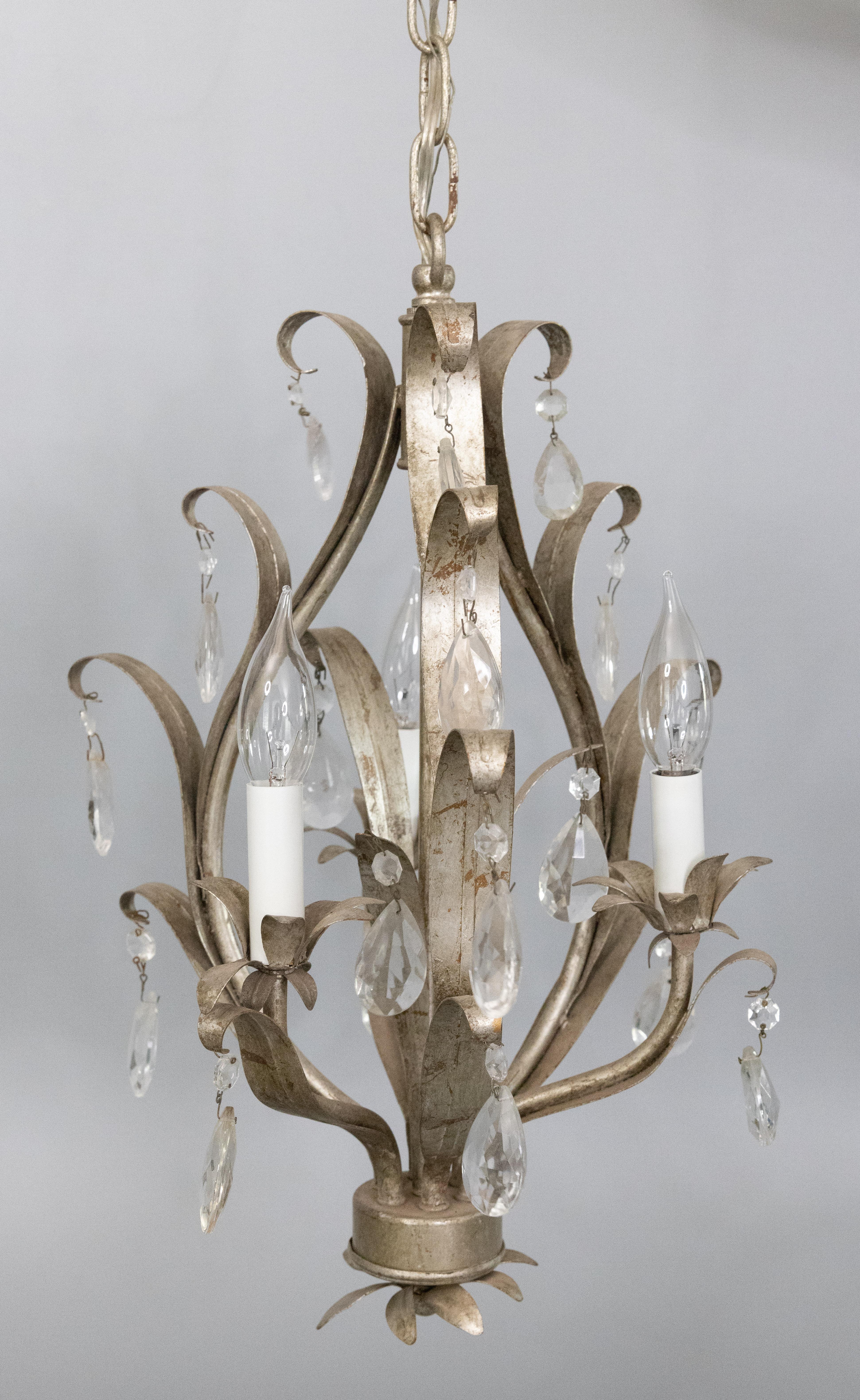 A stunning mid-20th century Italian silver tone gilded tole three light chandelier. This gorgeous chandelier has crystals and scrolling leaves in a beautiful silver gilt patina. It's in excellent working condition and comes with the original ceiling