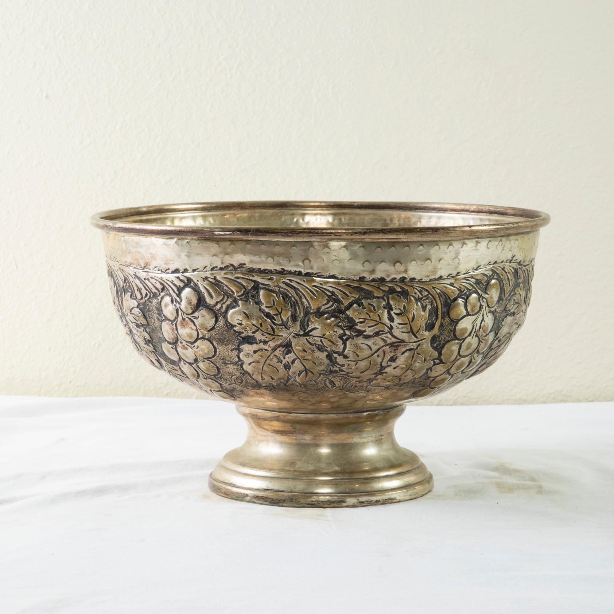This large mid-twentieth century Italian hotel champagne bucket features a hand hammered repousse grapes and grape leaf motif. The bucket rests on a footed base and can accommodate up to three bottles. The quintessential bar piece, this large