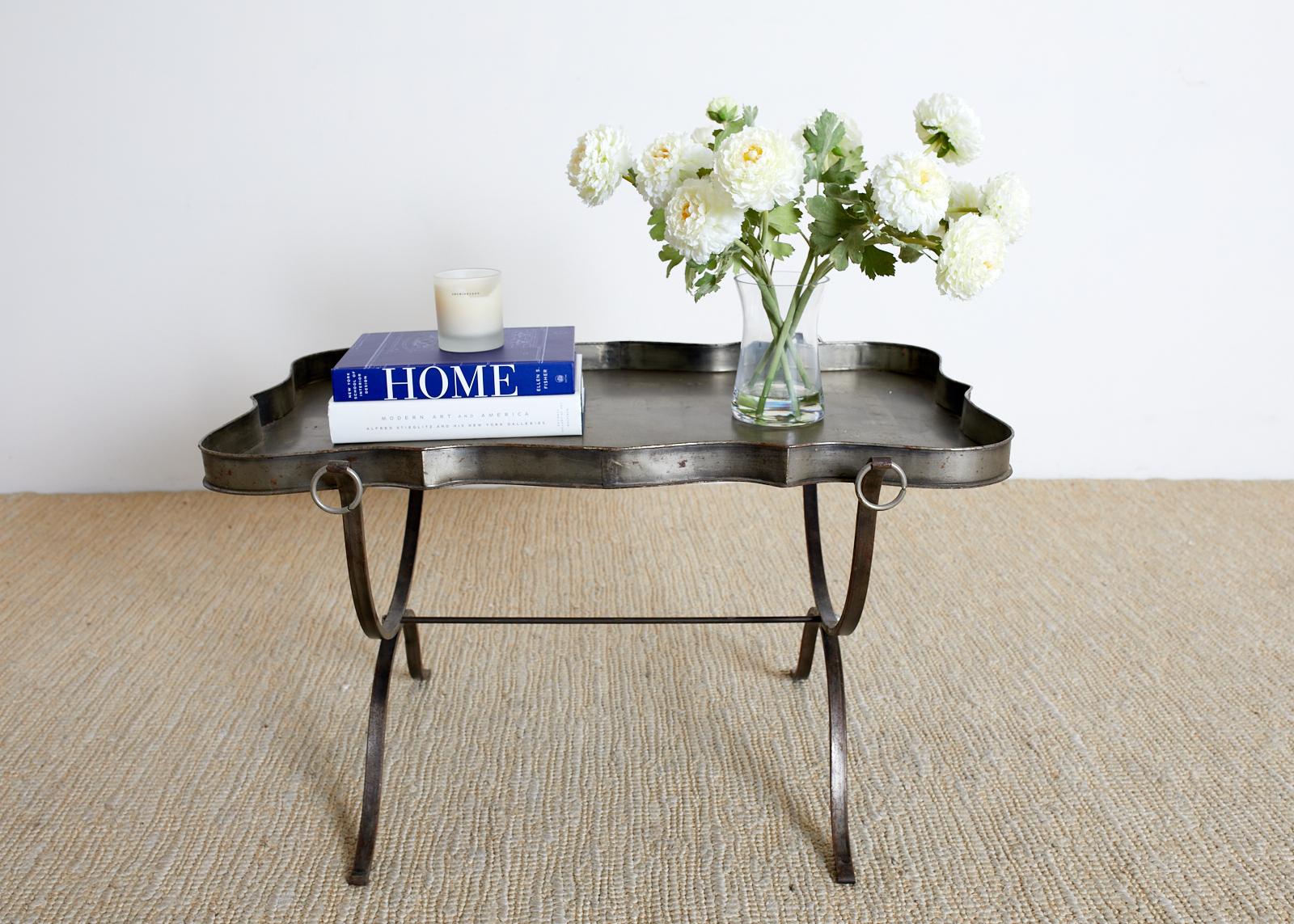 Mid-Century Modern Italian tole tray table constructed from silvered metal with an aged metal patina. Features a removable tray top with a serpentine edge and decorated with a painted bottom having a scroll motif. The X-form or curvle style base has