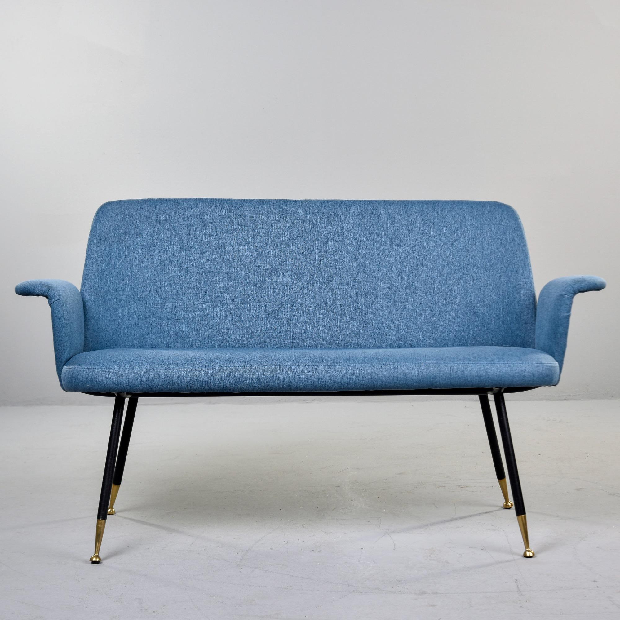 Found in Italy, this small upholstered settee dates from the 1950s. The sofa features simple lines with curved armrests and slender, tapered black iron legs and brass-tipped feet. Reupholstered in medium blue fabric by the Italian dealer we acquired