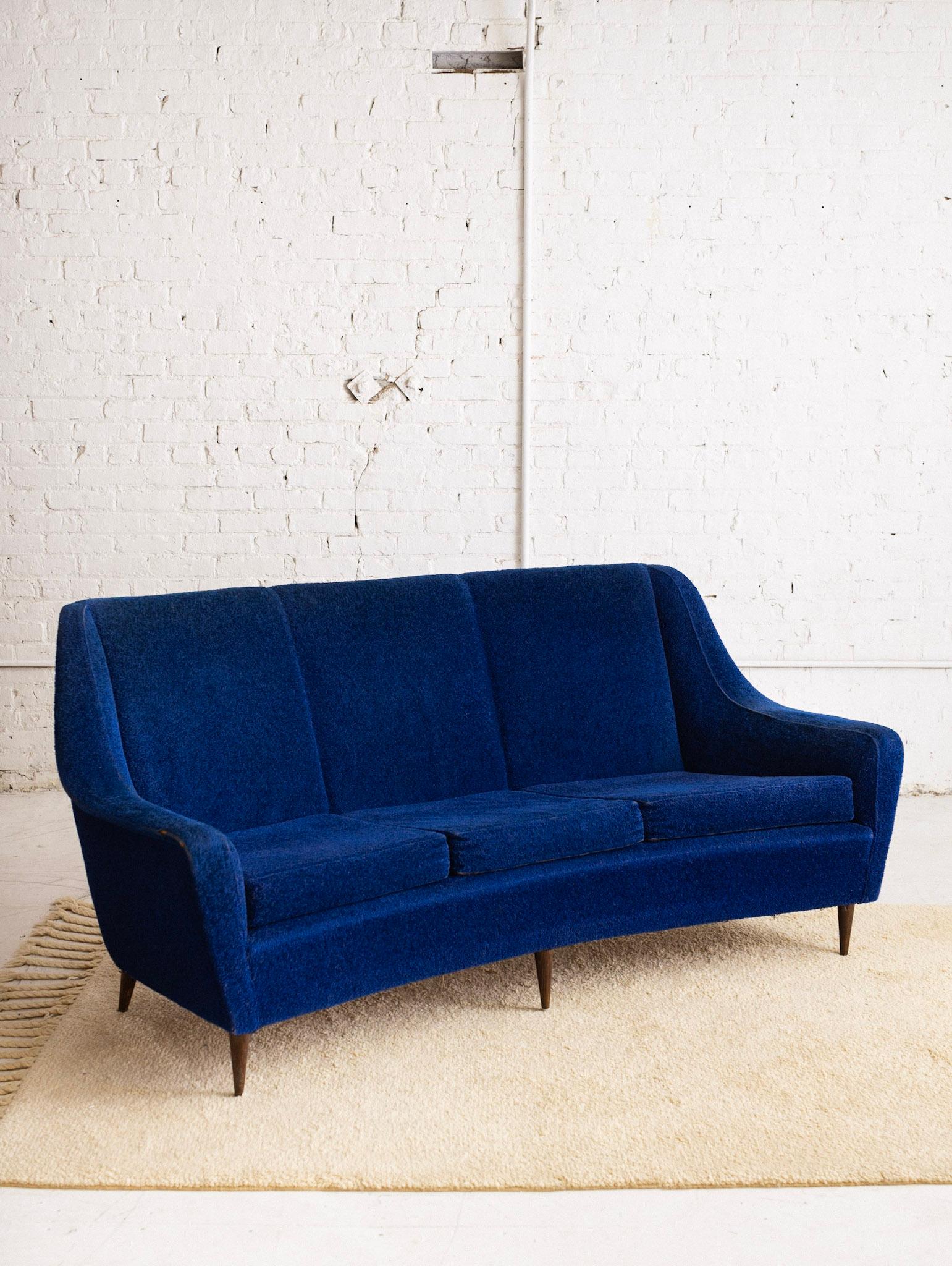 Italian Mid-Century Modern sofa in original cobalt blue boucle. Reversible floral pattern on seat cushions. Curved back. Tapered wood feet. Sourced in Northern Italy. This piece is recommended for reupholstery.