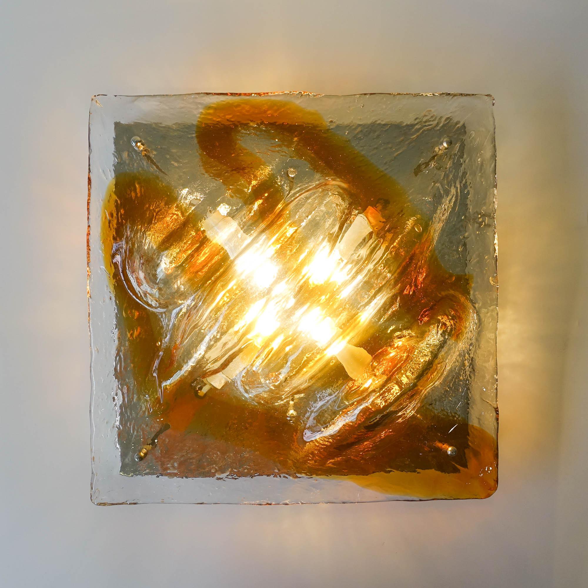 This sconce was designed and produced by Mazzega in Italy, during the 1960's. It has a thick wavy amber and clear Murano glass mounted on a chrome wall plate. It is a solid hand-blown Murano glass with some curves that gives an almost tridimensional