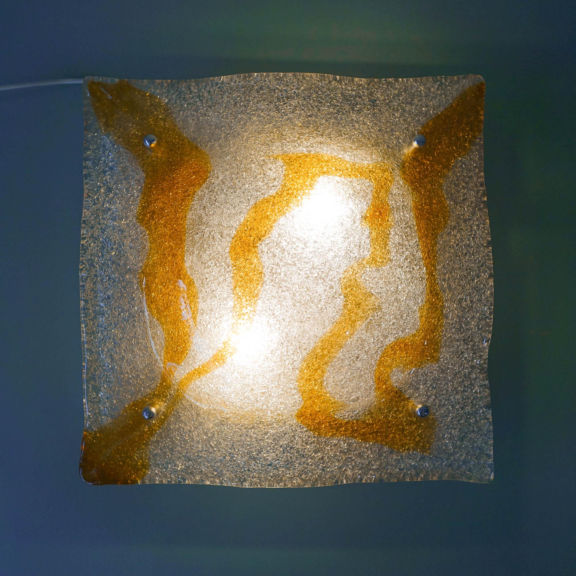 This sconce was designed by Toni Zuccheri for Mazzega in Italy, during the 1960's. It has a thick wavy amber and clear Murano glass mounted on a chrome wall plate. The glass is handmade with small bubbles (pulegoso) inside the glass and sprinkled