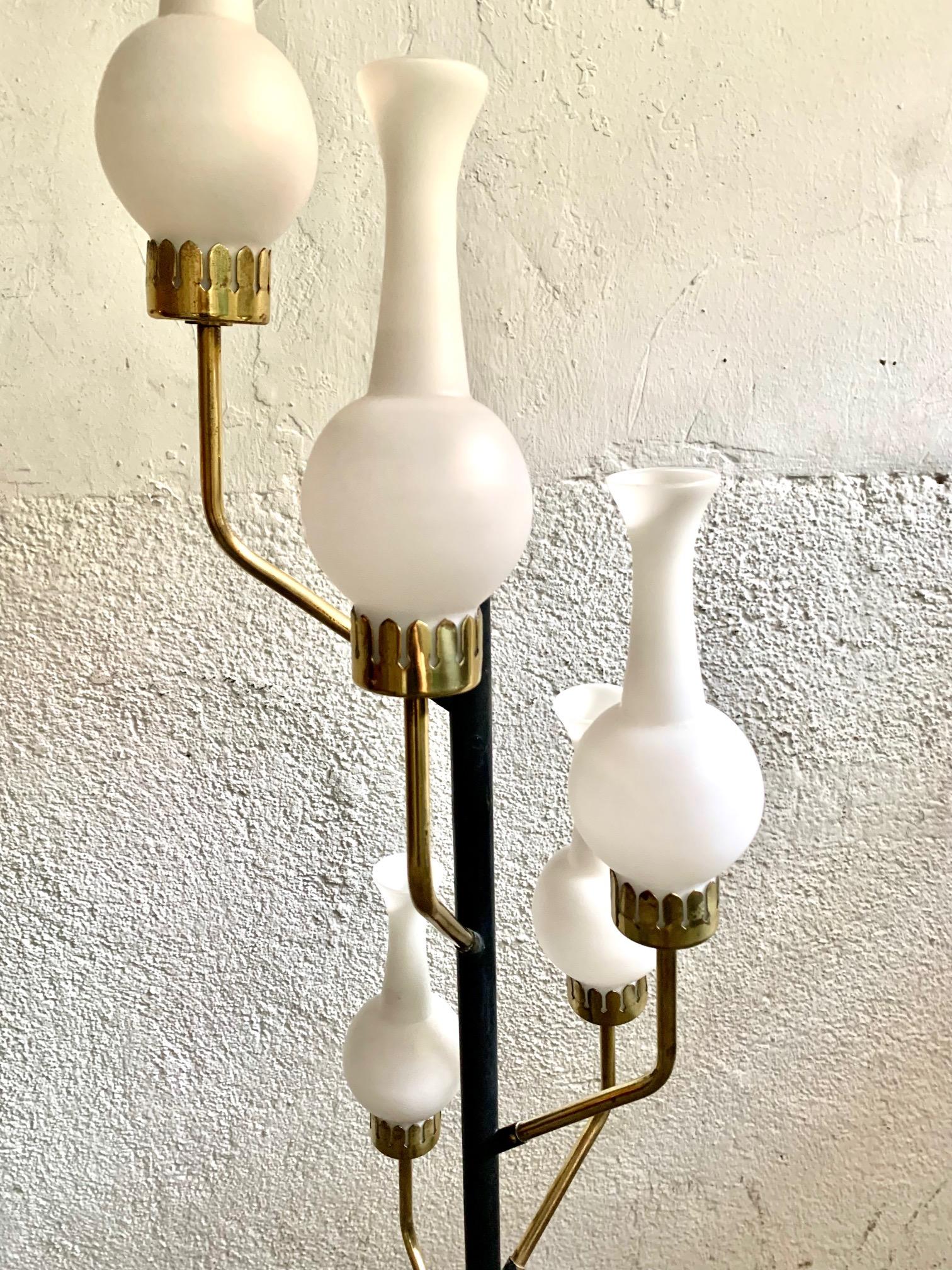 Italian floor lamp, from the 50s and in the style of the well-known Stilnovo, the lamp has a tripod foot from which comes a column with five golden brass arms where the light bulbs are supported, the five arms end with lamp sahdes of white opaline