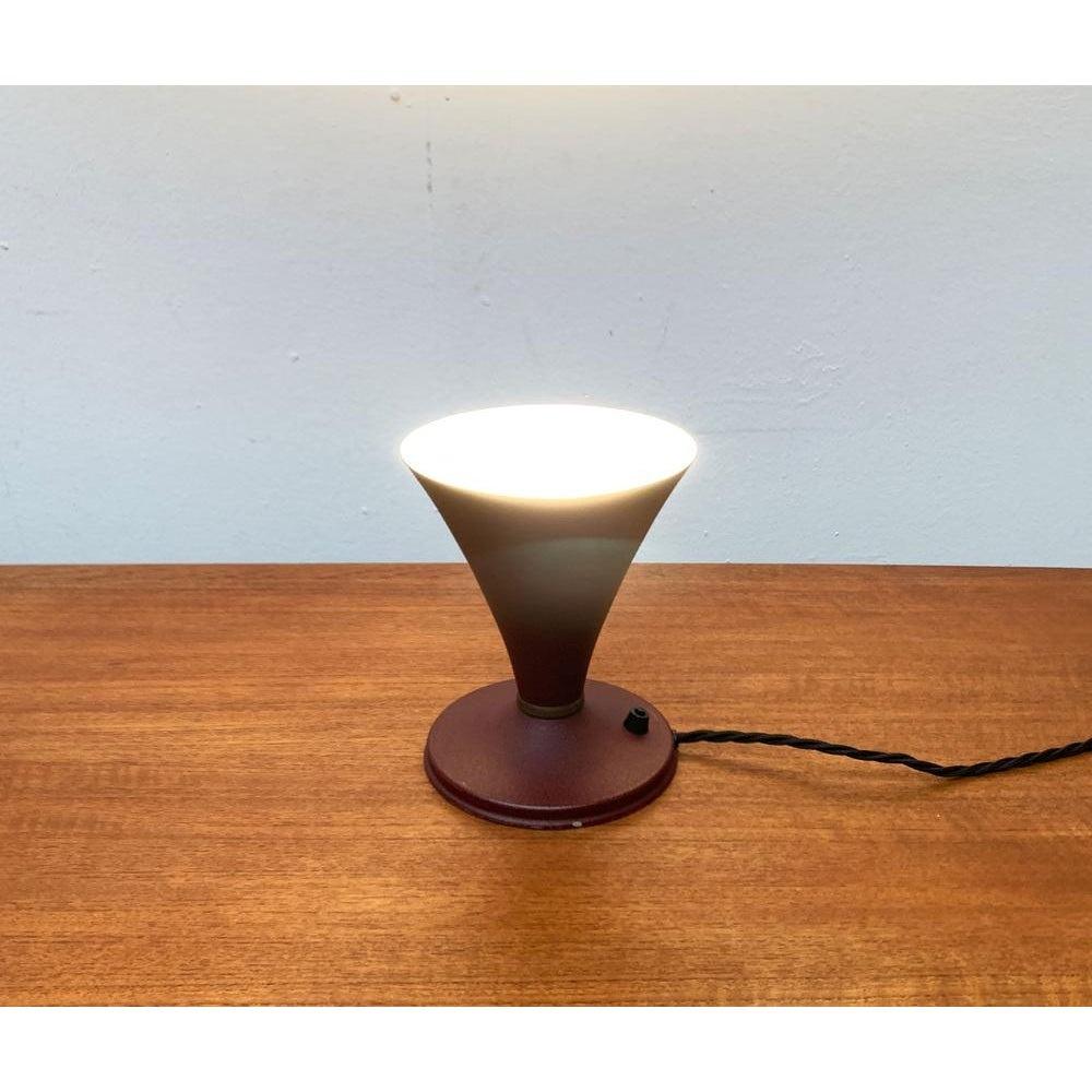 Mid Century table lamp from Italy.

The lamp shows a classic funnel shape. The shape of the umbrella rejuvenates close to the bottom and then widen again to train a foot. Foot and umbrella are deposed with a brass ring. The lamp is covered with dark