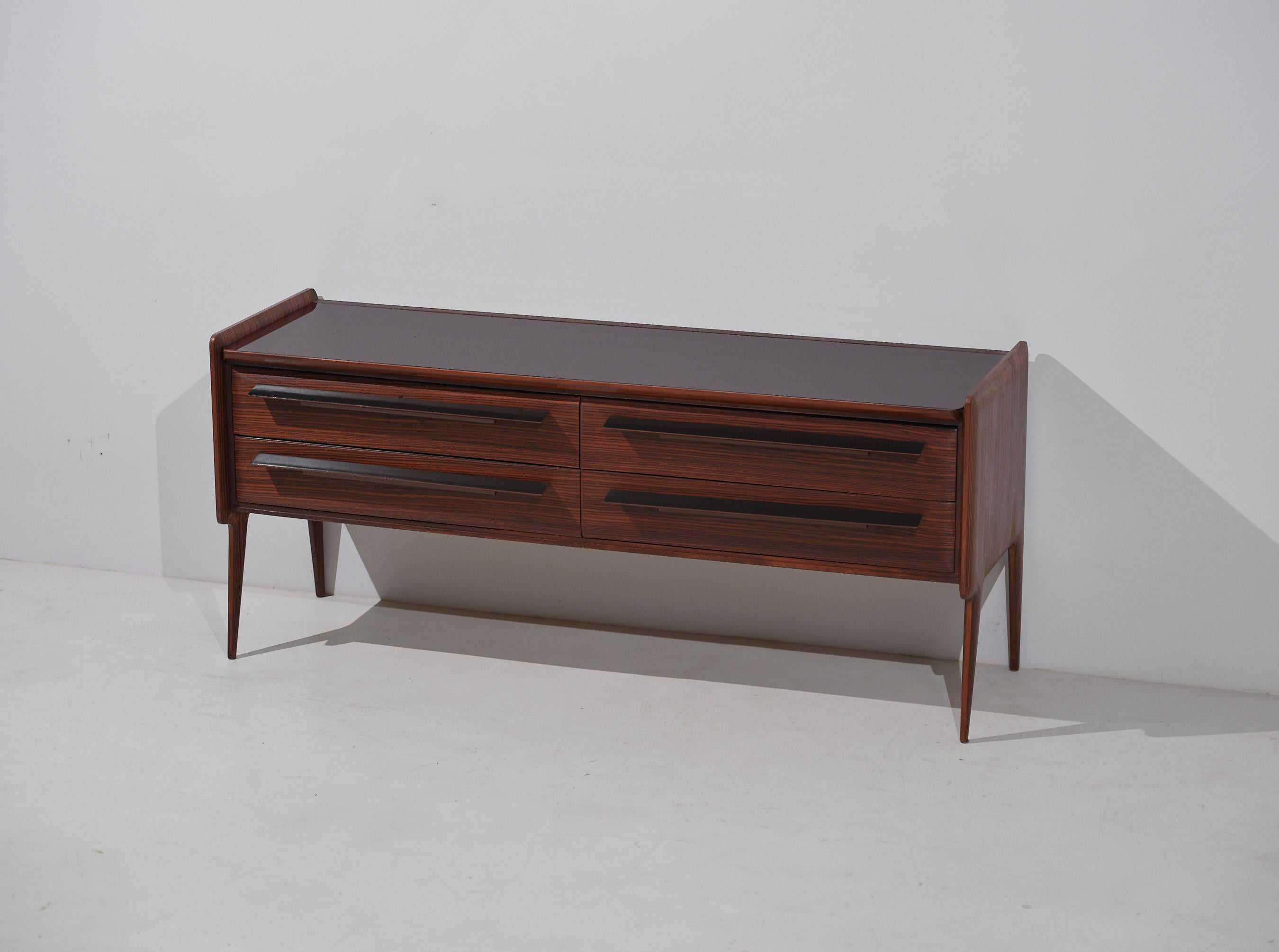This mid-century dresser, designed and crafted in Italy during the 1950s, beautifully combines functionality with refined aesthetics. The piece features a dark brown back-painted glass top which harmoniously complements the striped exotic wood
