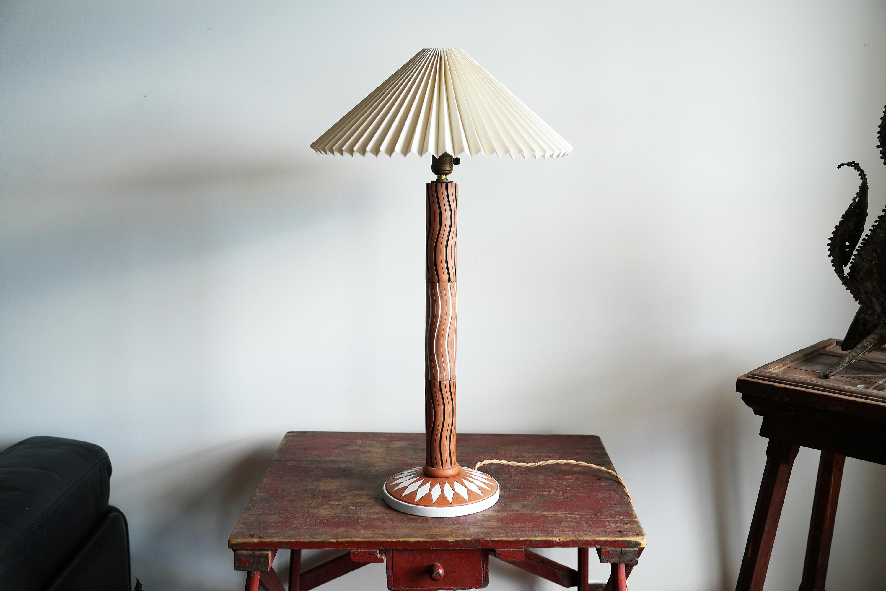 This is a graphic mid century Italian terracotta lamp with pleated shade. The body of the lamp is incised with alternating black and white waves with the base having a white glazed foot and diamond pattern. Signed on underside 'Beth Weissman,