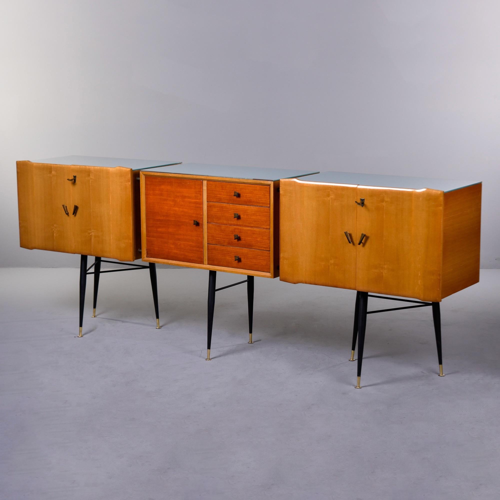 Found in Italy, this three segment buffet dates from the late 1950s. Two blonde cabinet sections flank a center bank of four drawers and small cabinet in a contrasting stain. The black metal base has eight tapered legs with brass feet and each