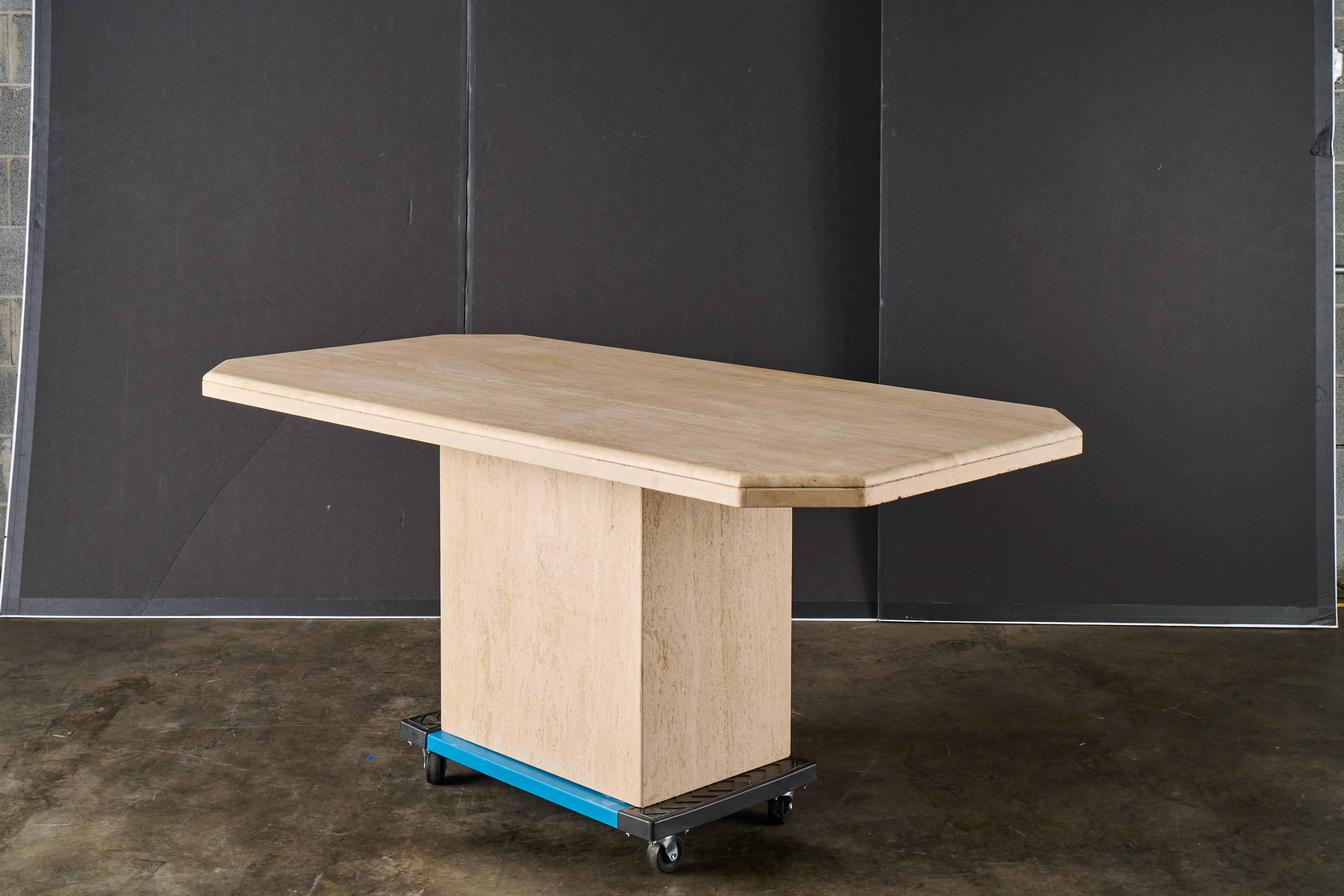 Una llamativa mesa de comedor de travertino de la modernidad de mediados de siglo, fabricada en Italia hacia la década de 1970. La mesa tiene una presencia escultural y monolítica, con un grueso tablero rectangular de bordes biselados que descansa