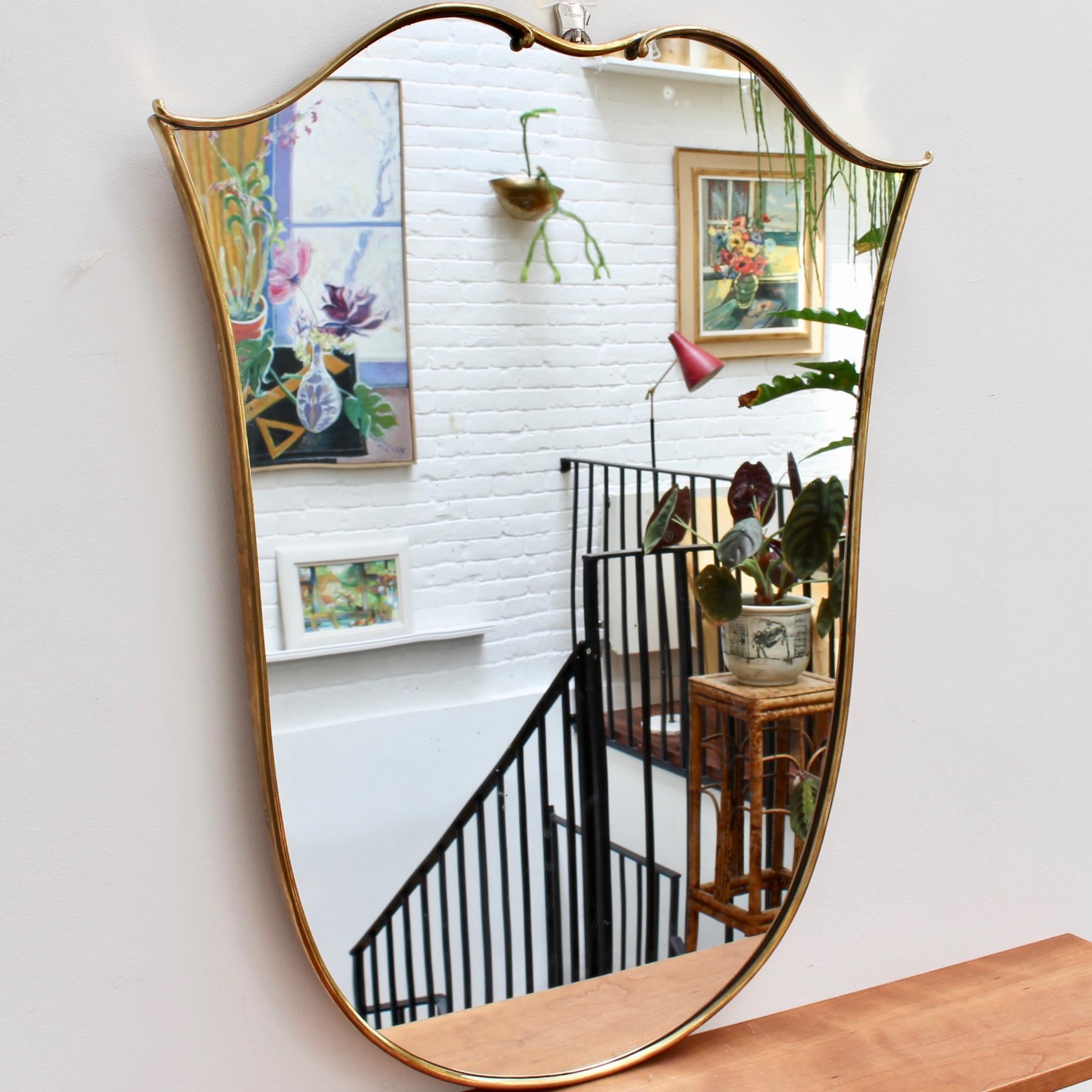 Midcentury Italian wall mirror with brass frame (circa 1950s). This mirror has sensuous curves yet retains its solidity and imposing good looks. The tulip-shape is topped with two special flourishes rarely found in this style of mirror. It is in