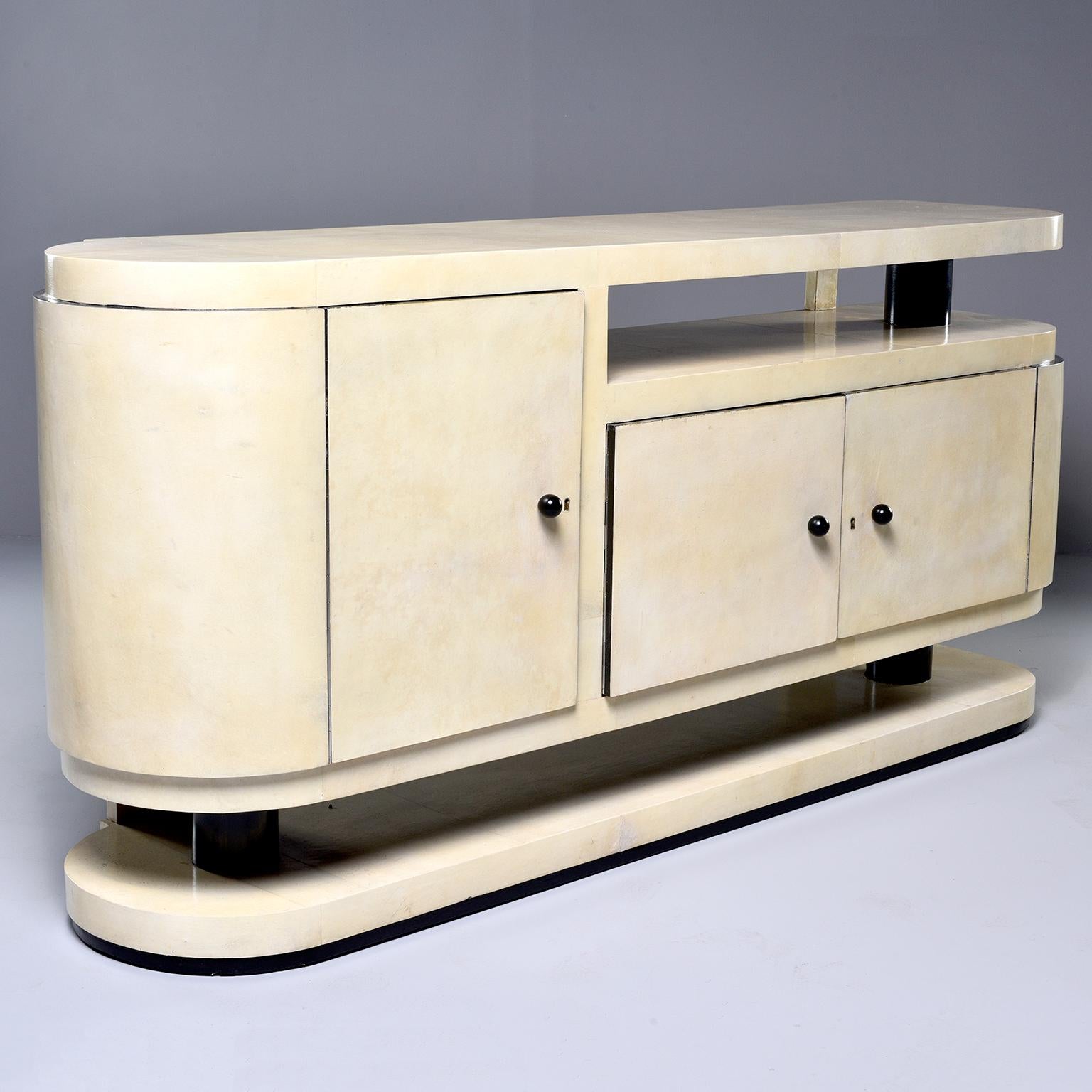 Italian sideboard or buffet is wood and completely covered in cream colored vellum, circa 1960s. One side has a tall cabinet with one internal shelf and the other side has a low, two-door cabinet. The cabinet appears to float over the curved