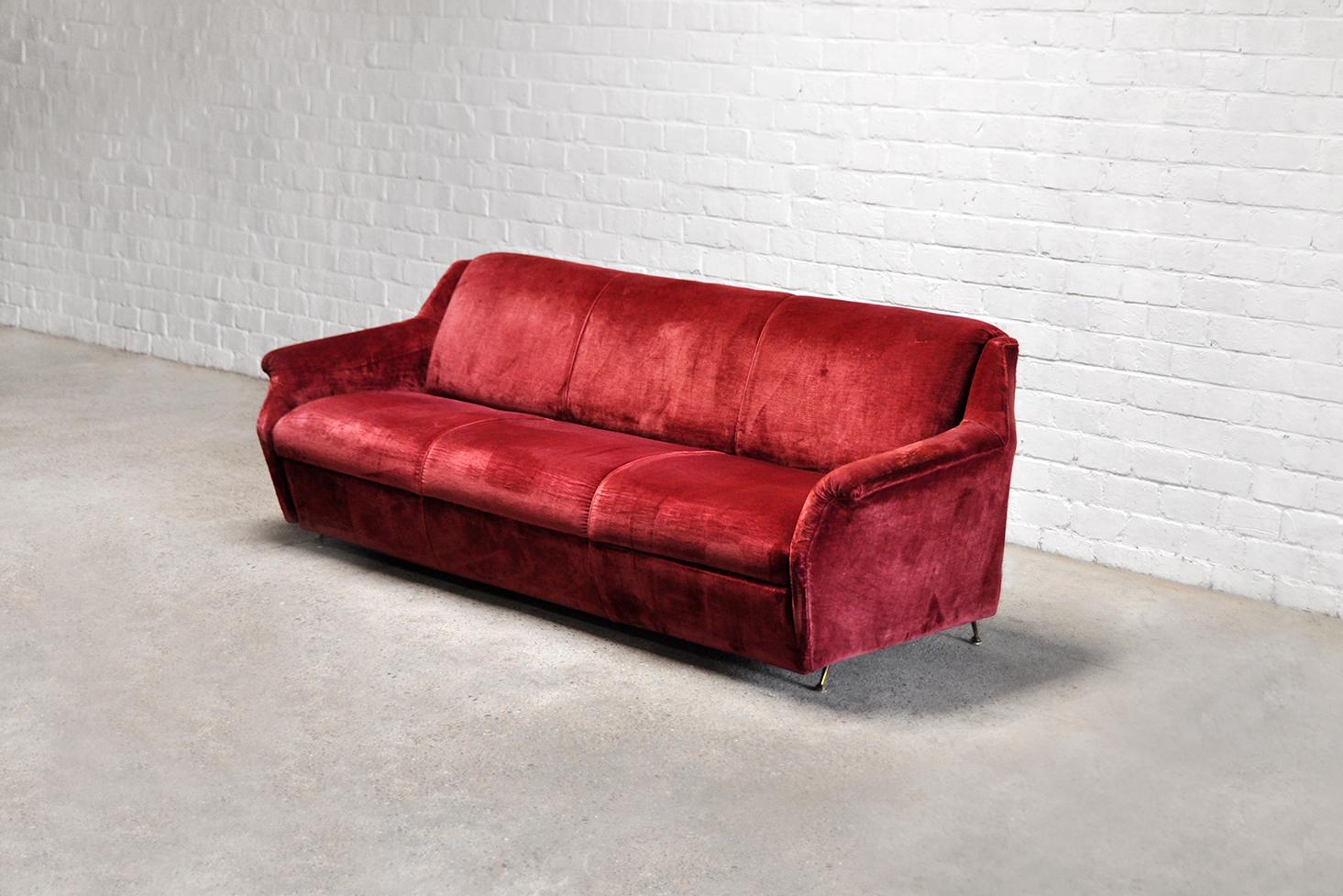 A mid-century italian designer sofa from the 1950’s. Upholstered in a maroon red velvet with an interesting angular design and splayed patinated brass legs. Beatifully shaped appearance and form.

Wear consistent with age and use. The original