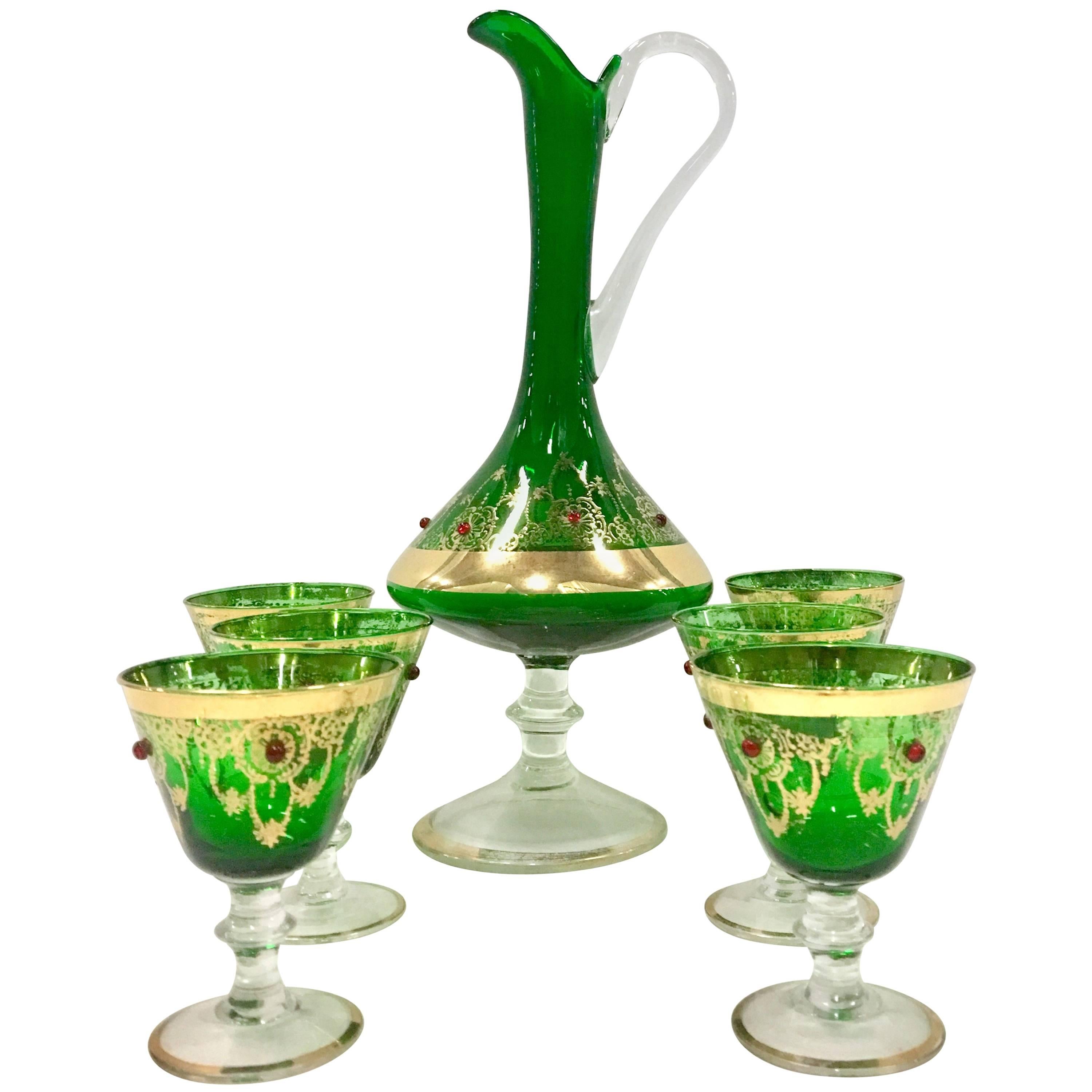 Midcentury Italian 22-karat gold and emerald green Venetian blown glass drinks set of seven pieces. This hand painted seven piece set features a spouted and applied handled footed pitcher and six cordial footed stem glasses. The 22-karat gold scroll