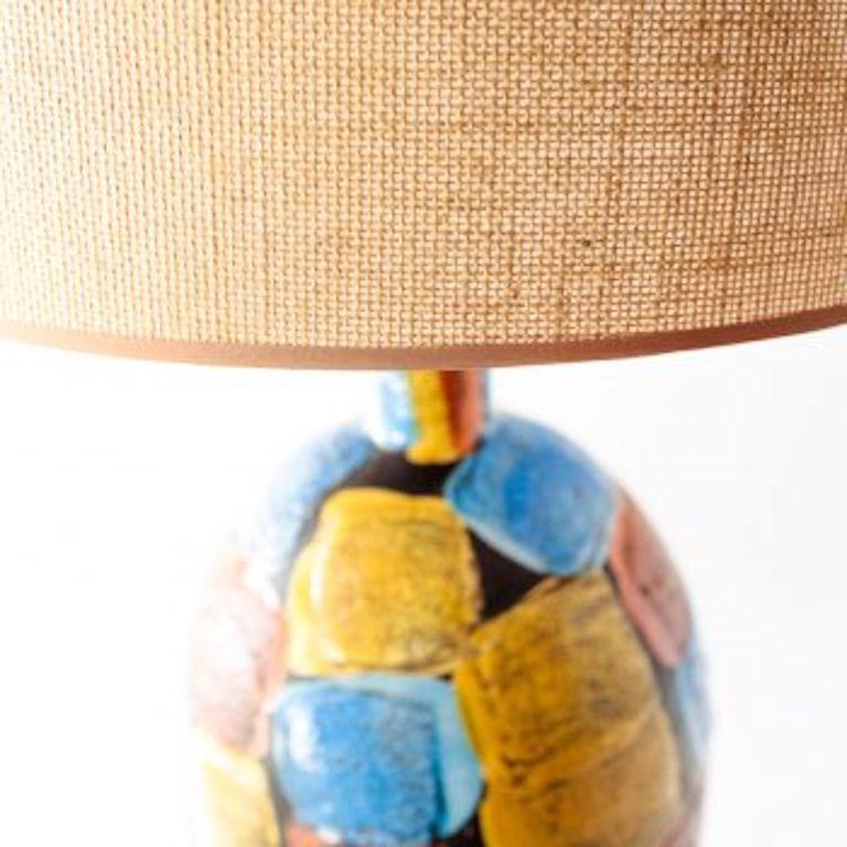 Volcanic glazed ceramic lamp made in Italy. Bright blue, ochre, and burnt orange overall patchwork design. Textured surface. Wooden base in a dark walnut finish. Rewired with a braided nylon cord. New burlap tapered drum shade.