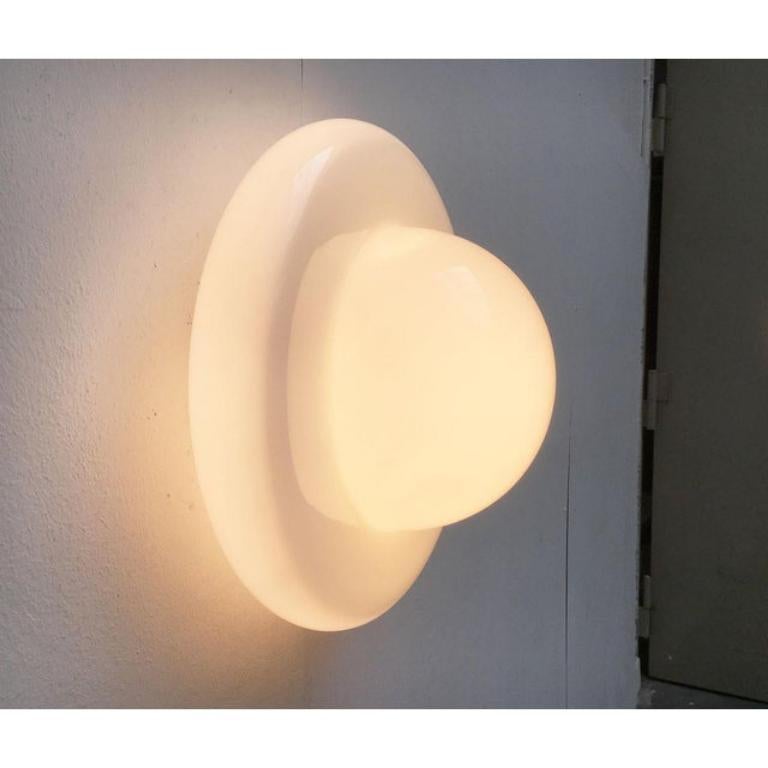 Lampada da soffitto o da parete di origine italiana.
 Colpiscono le curve morbide del diffusore. È interamente in vetro e si monta sulla piastra di base con 3 viti. La base è in metallo e contrasta per materiale e colore con il vetro bianco. Fino a
