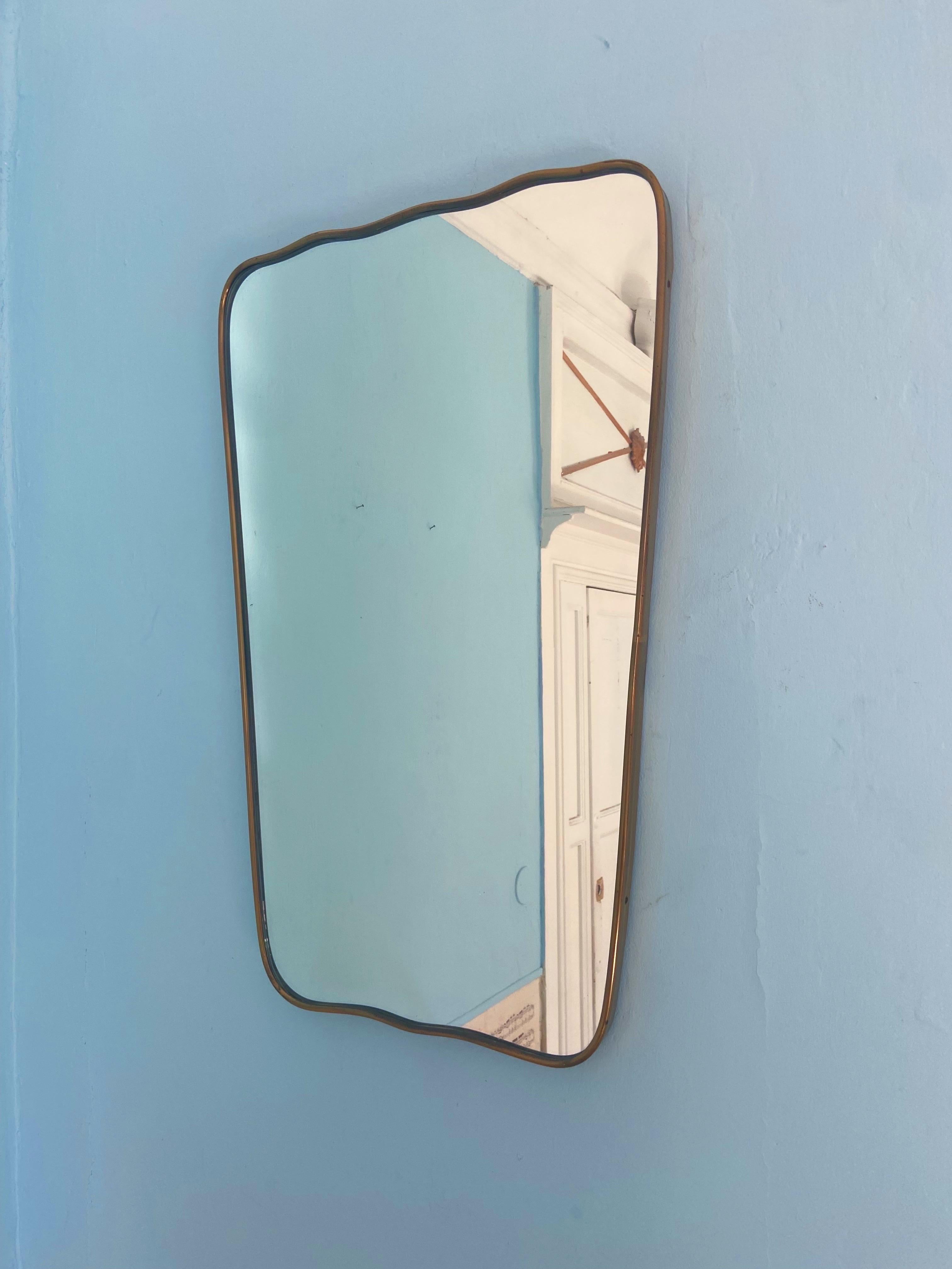 Espejo de pared italiano de mediados de siglo diseñado por Gio Ponti. Espejo original sin restaurar con marco de latón (hacia 1950). Forma curvilínea y característica muy elegante. La parte trasera es de madera maciza y conserva los ganchos