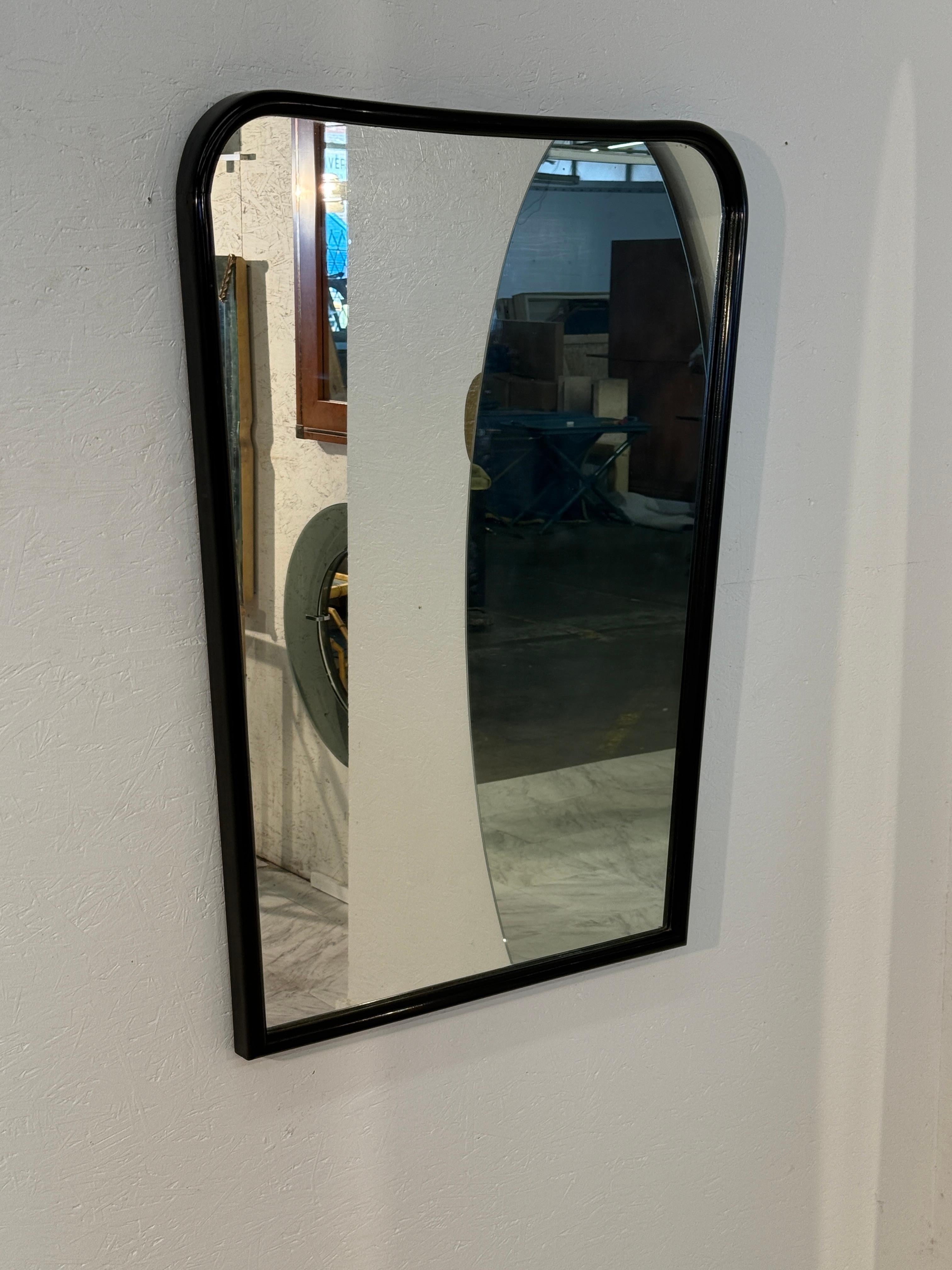 Questo specchio da parete unico e moderno di metà secolo presenta un'elegante cornice nera con angoli morbidamente arrotondati. Lo specchio stesso ha un taglio artistico e curvo che crea un riflesso scultoreo di grande effetto, aggiungendo