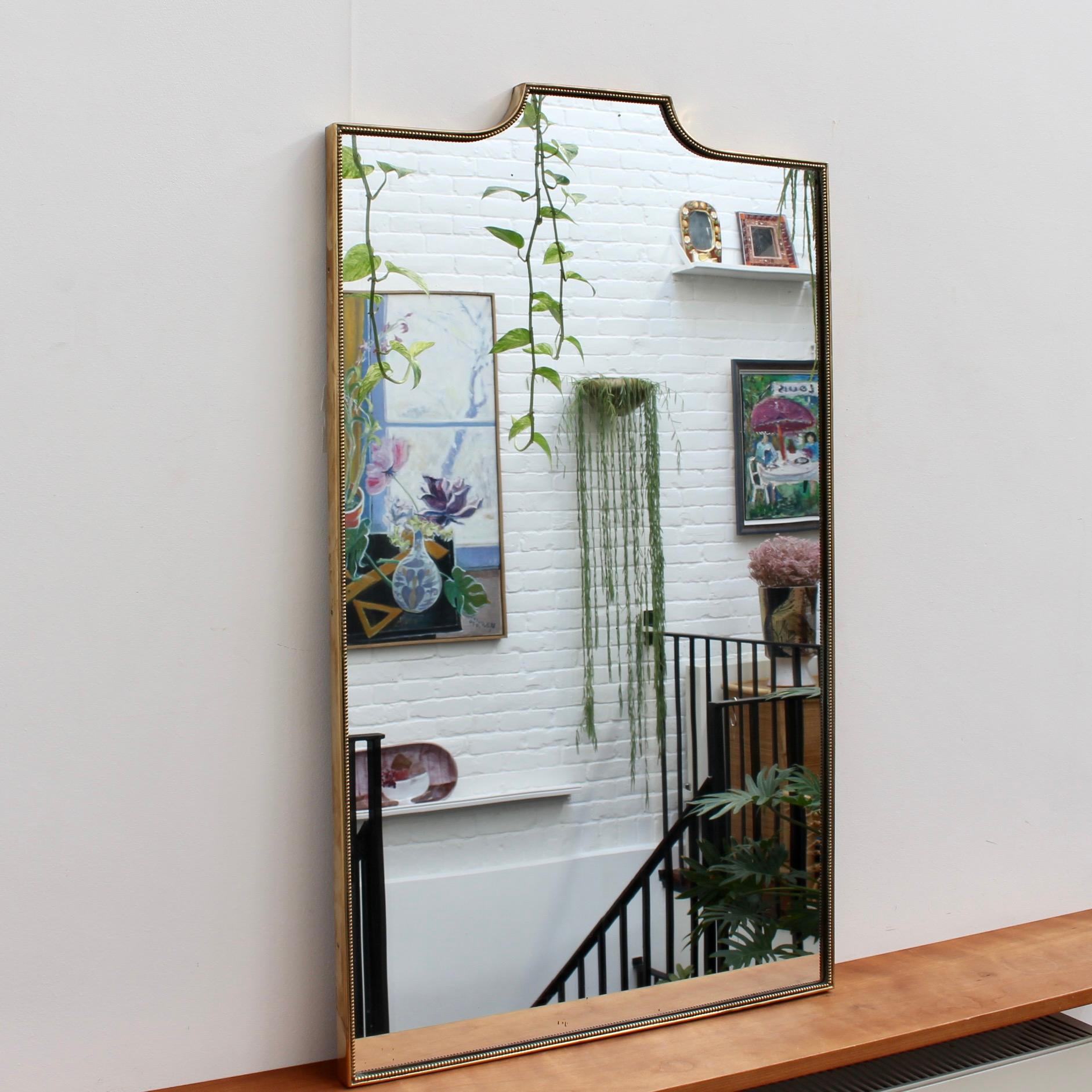 Mid-century Italian wall mirror with brass frame (circa 1950s). The mirror is large, rectangular in shape, smart and distinctive in a modern Gio Ponti style with a distinctive beading outlining the frame. The mirror sports a curve leading to a
