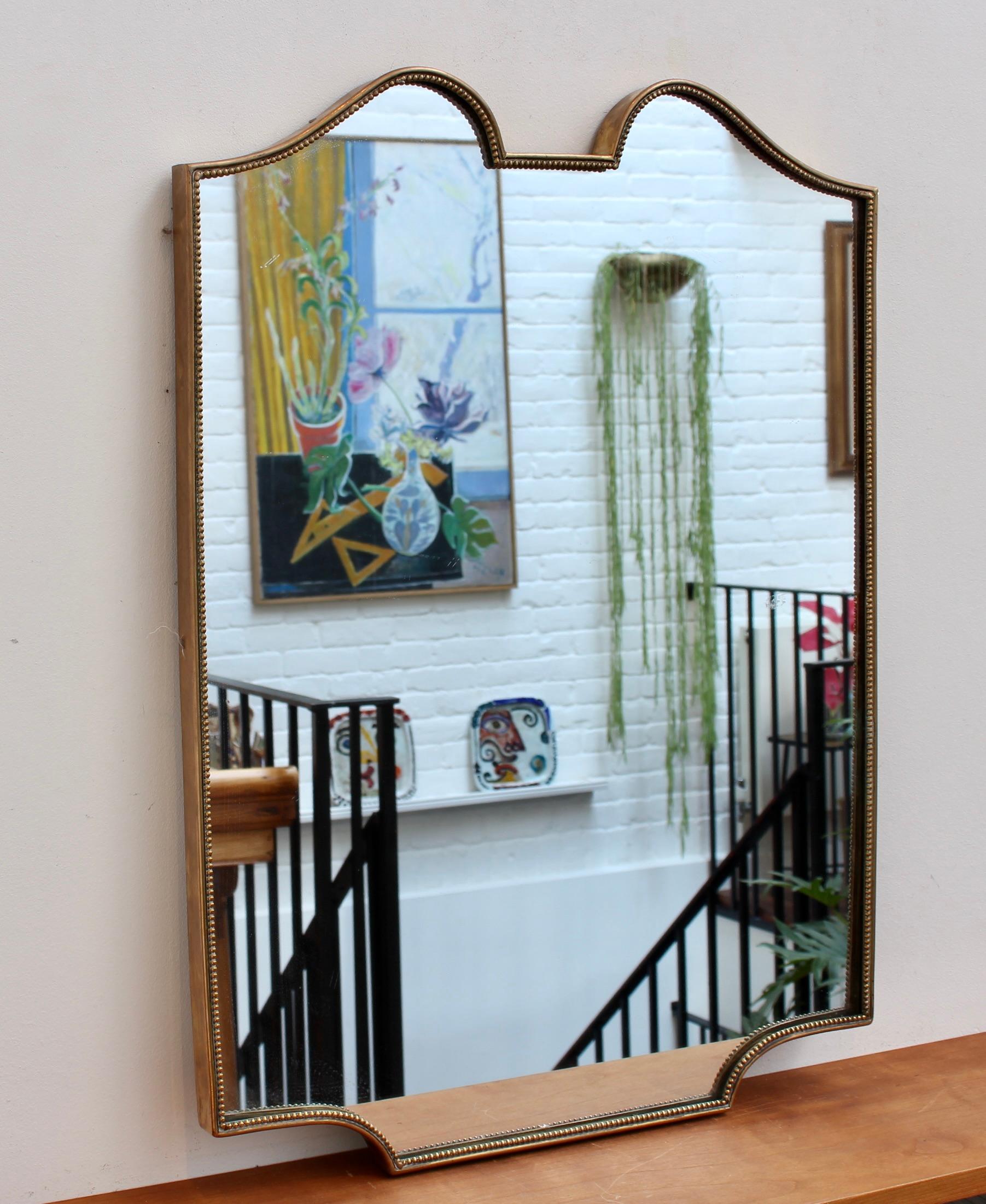 Mid-century Italian wall mirror in a brass frame with beading (circa 1950s). The smart, sturdy mirror sports a very original and delightful shape. Like other mirrors in this style, they are always classically elegant and distinctive. In good overall