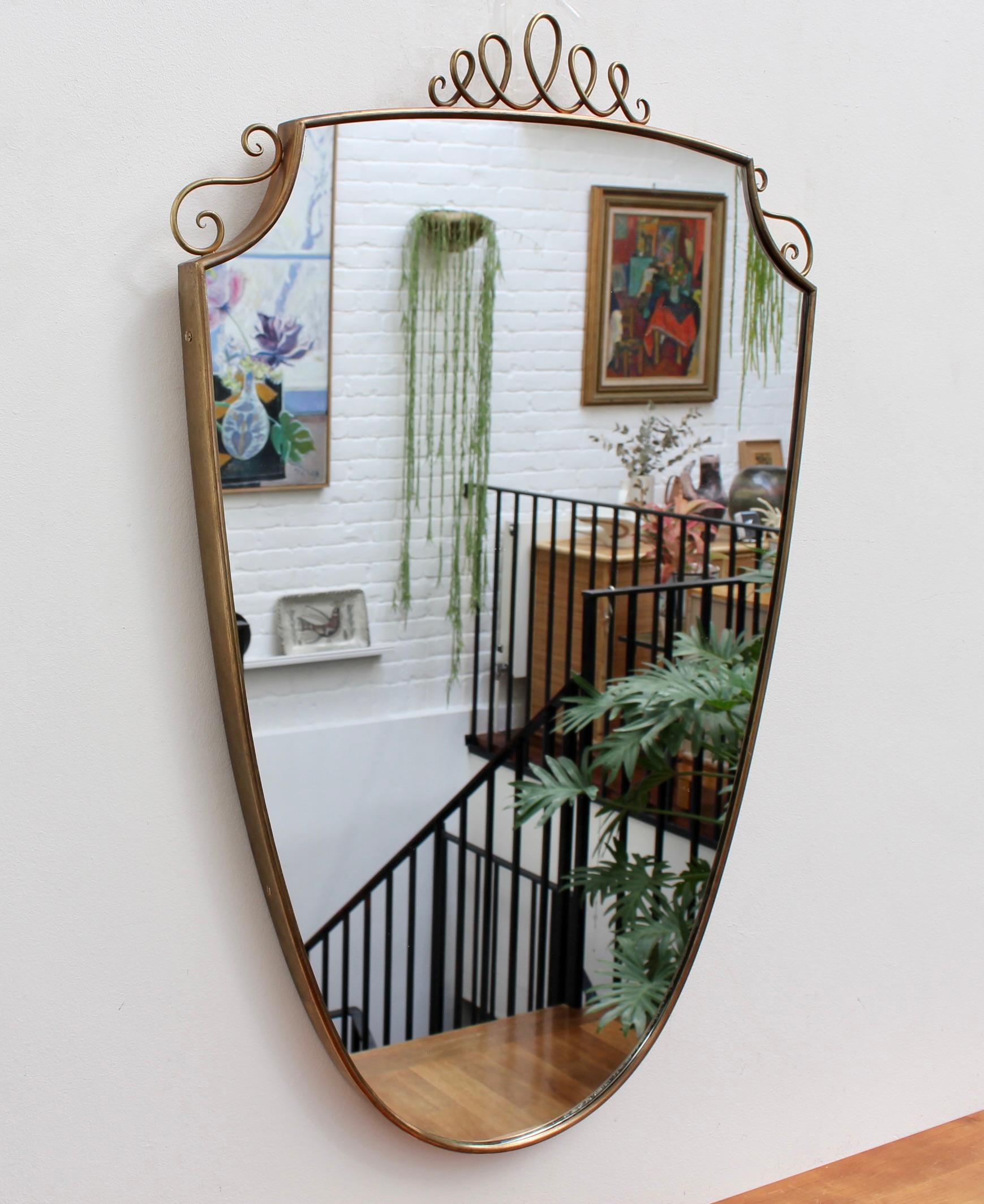 Mid-Century Italian wall mirror with brass frame and top flourish (circa 1950s). This mirror is simply elegant and characterful in a modern, Gio Ponti style. It is classically-shaped presenting a charming top flourish in the form of a decorative