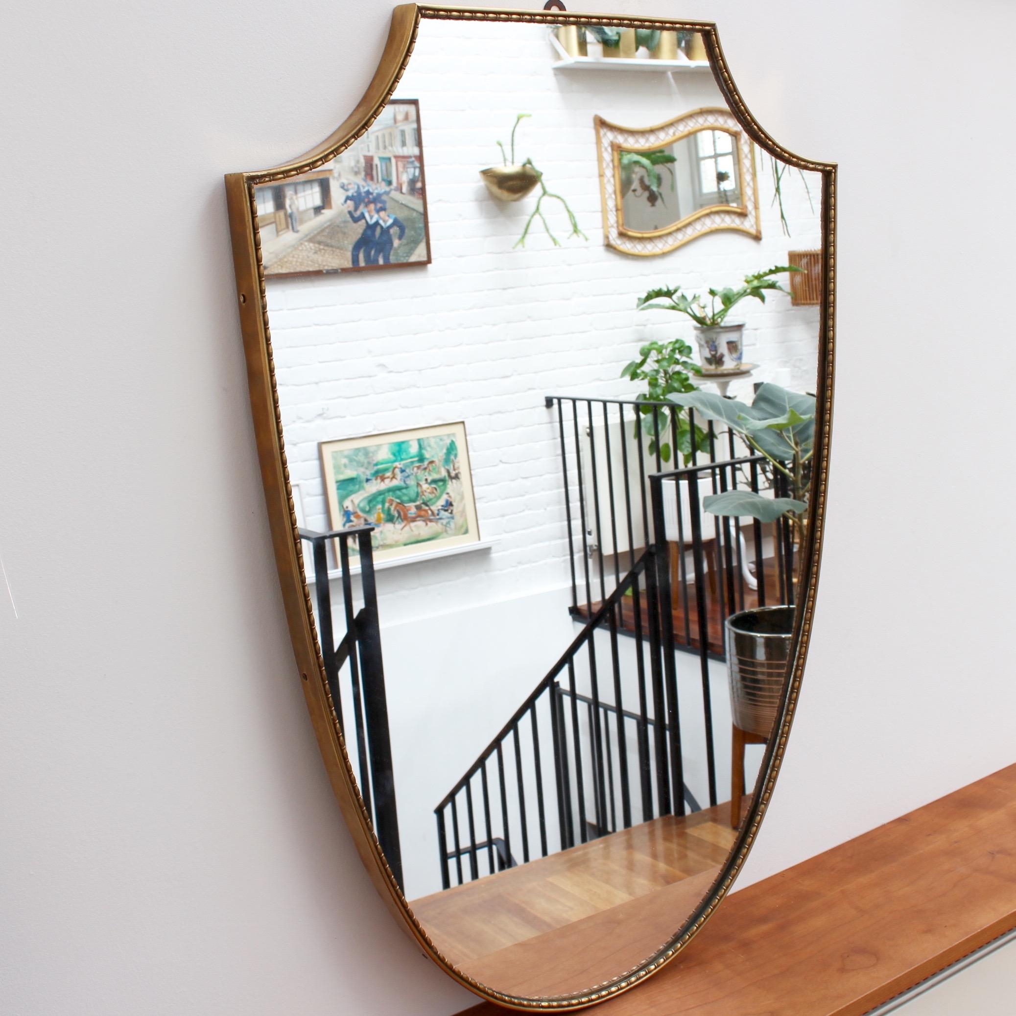 Midcentury Italian wall mirror with brass frame (circa 1950s). The mirror is large, crest-shaped, classically elegant with distinctive beading in a modern Gio Ponti style. This mirror is in good vintage condition. There are some evident but