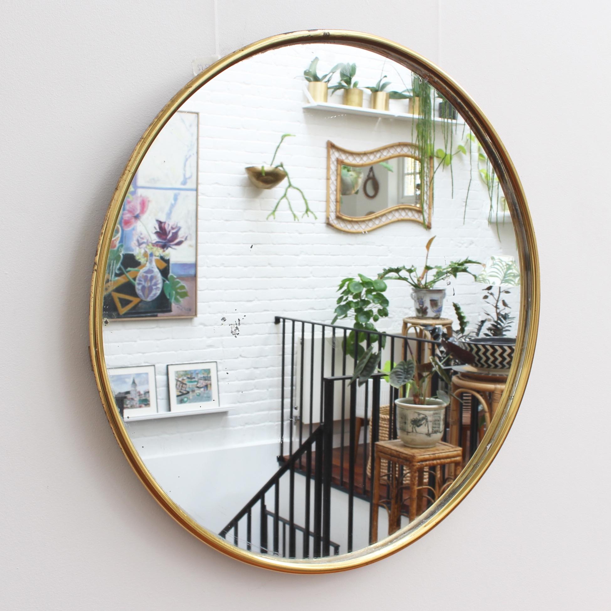 Midcentury Italian wall mirror with brass frame (circa 1950s). The mirror is perfectly round and porthole-shaped with a unique tubular brass frame. It is distinctive in a modern Gio Ponti style. The piece is in fair vintage condition with some