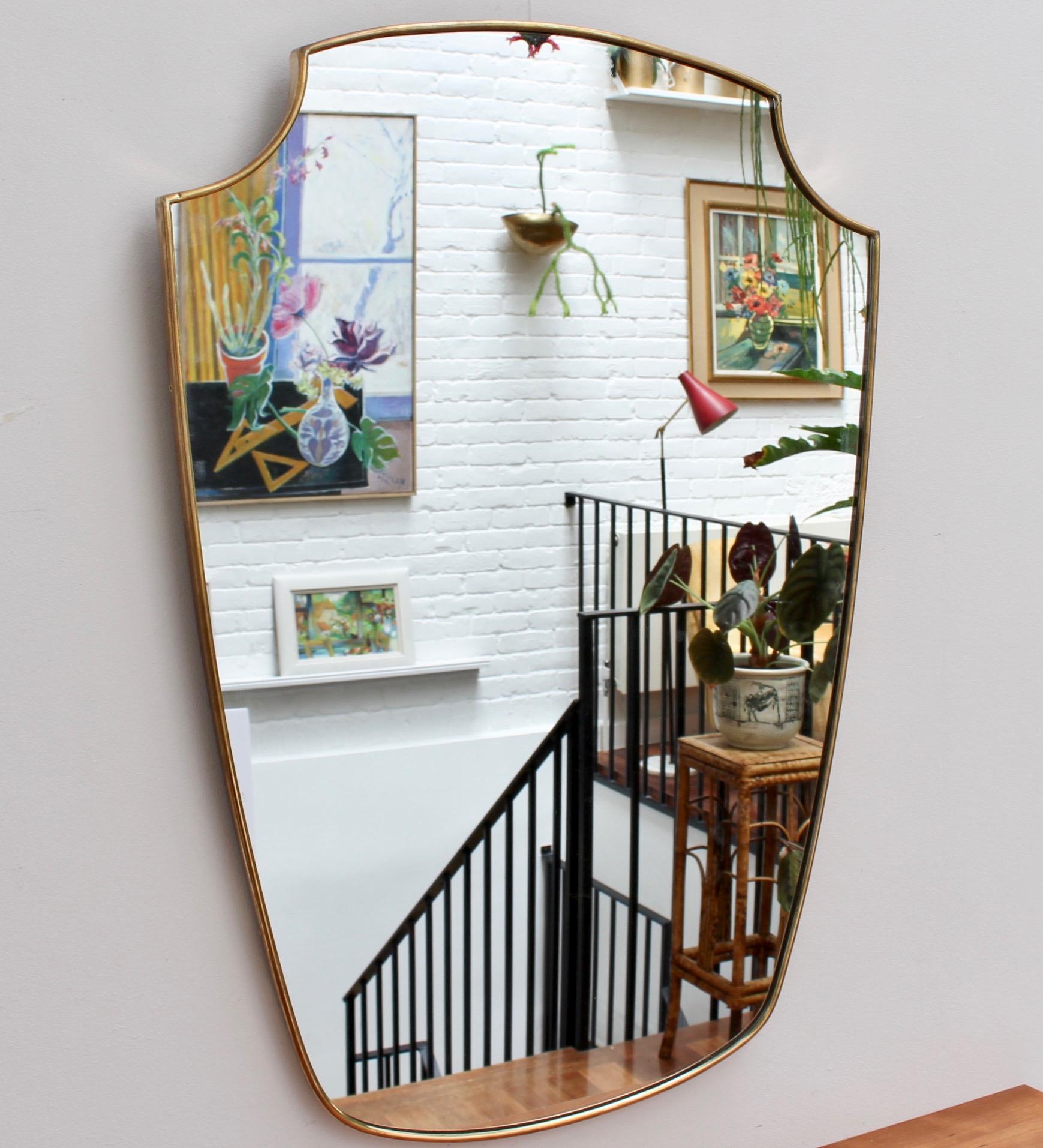 Midcentury Italian wall mirror with brass frame (circa 1950s). This mirror is simply elegant and characterful in a modern Gio Ponti style. It is crest-shaped and in good vintage condition. There is a characterful, aged patina on the brass frame