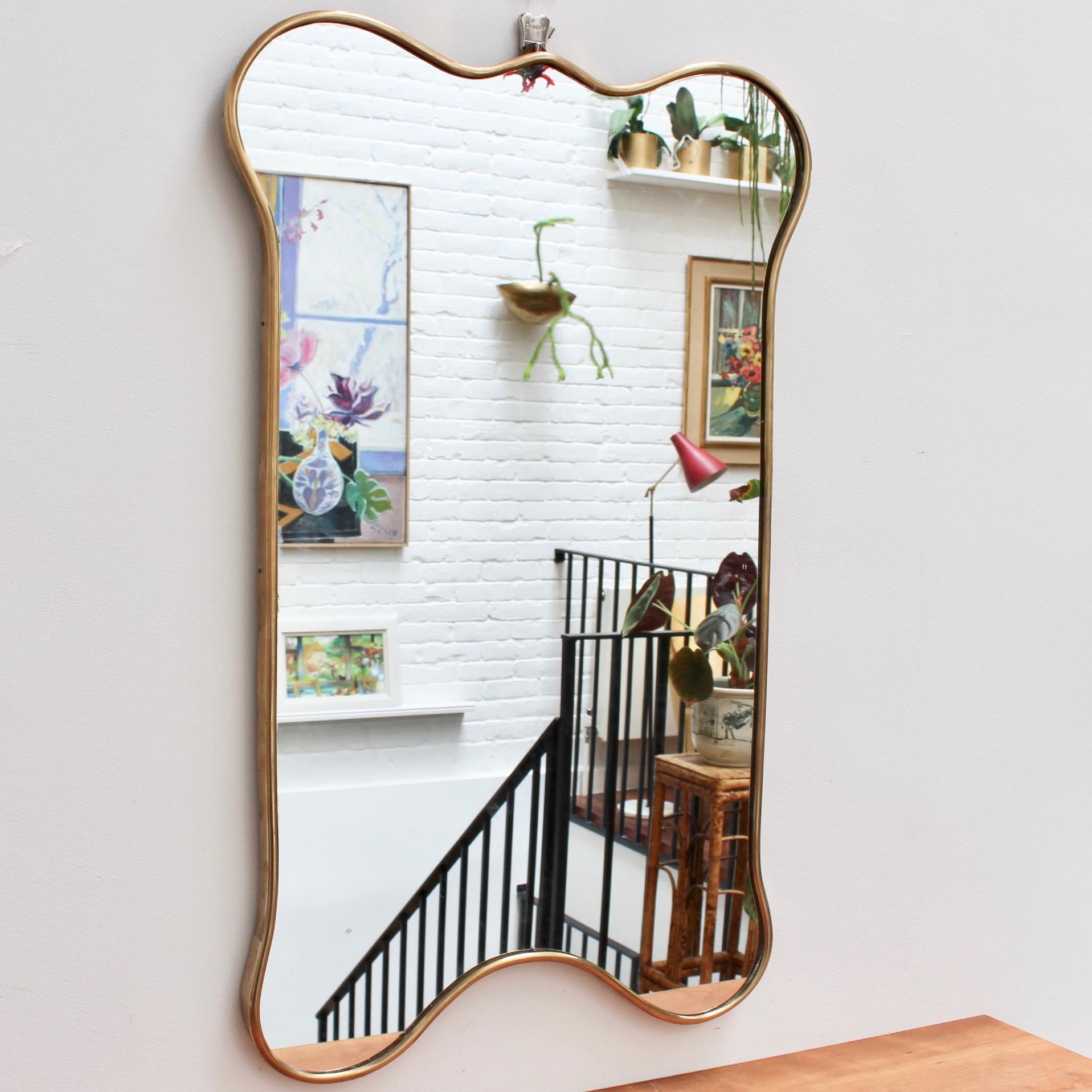 Midcentury Italian wall mirror with brass frame, (circa 1950s). This mirror has sensuous curves yet retains its solidity and imposing good looks. The vertical dog bone-shape features rounded edges on top and bottom with parallel lines in between. It